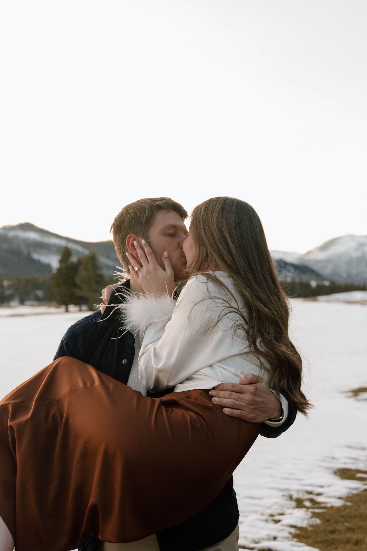 Intimate winter engagement photos with snow-capped mountains in the background.