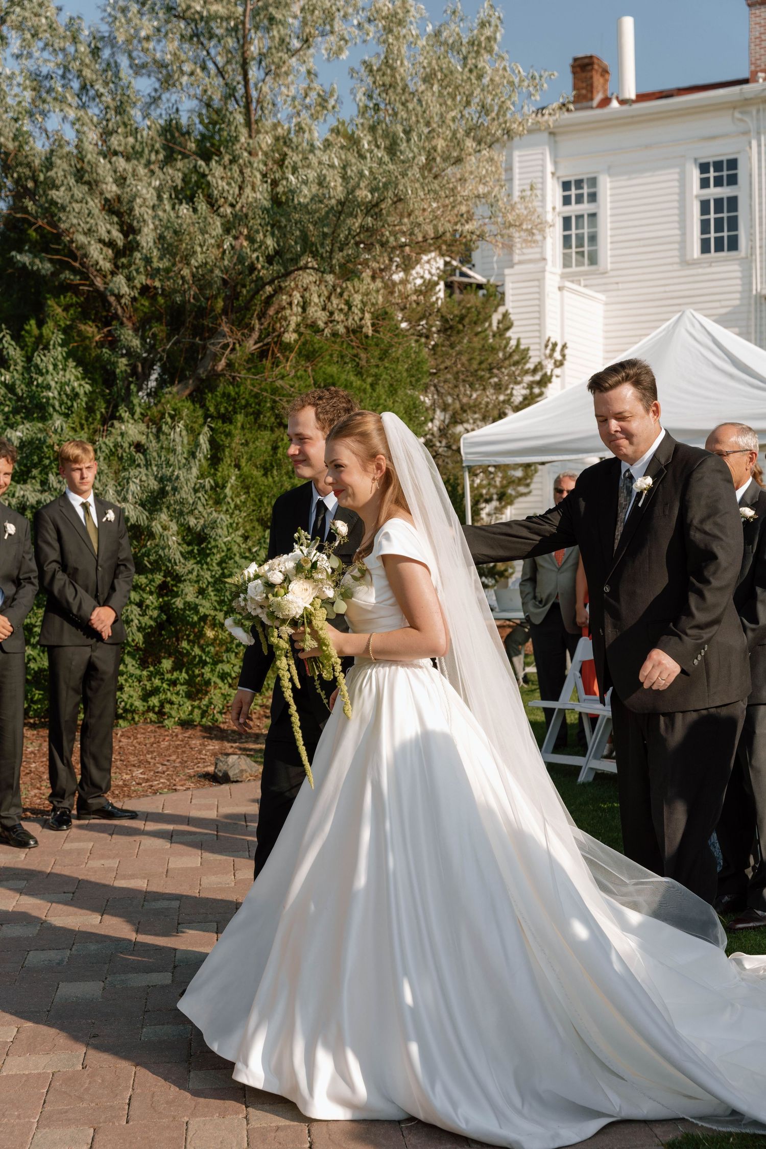 A wedding couple walks down a brick pathway during their outdoor ceremony.