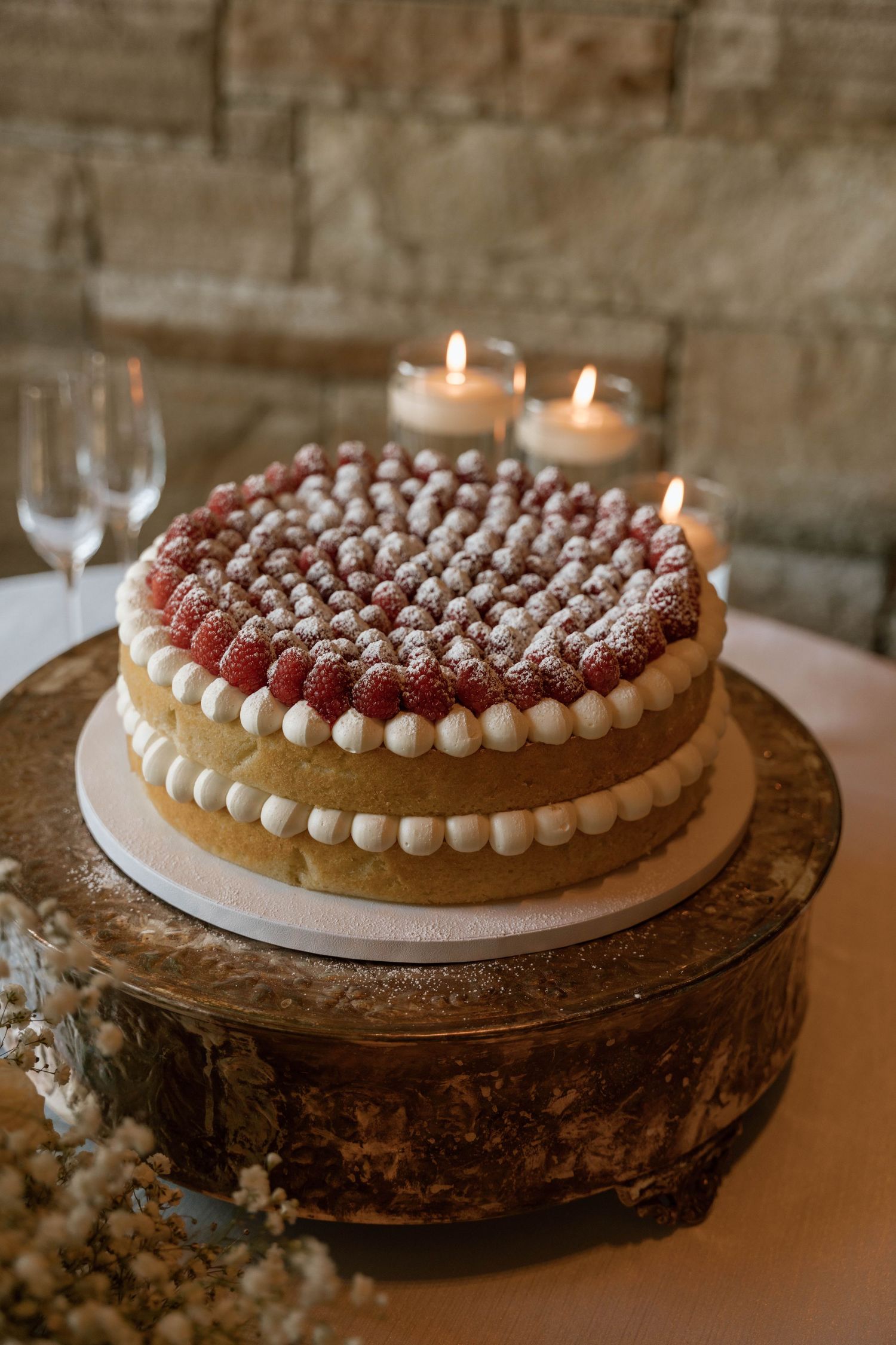 A beautifully decorated wedding tart with cream piping and raspberries displayed on a rustic wooden stand.