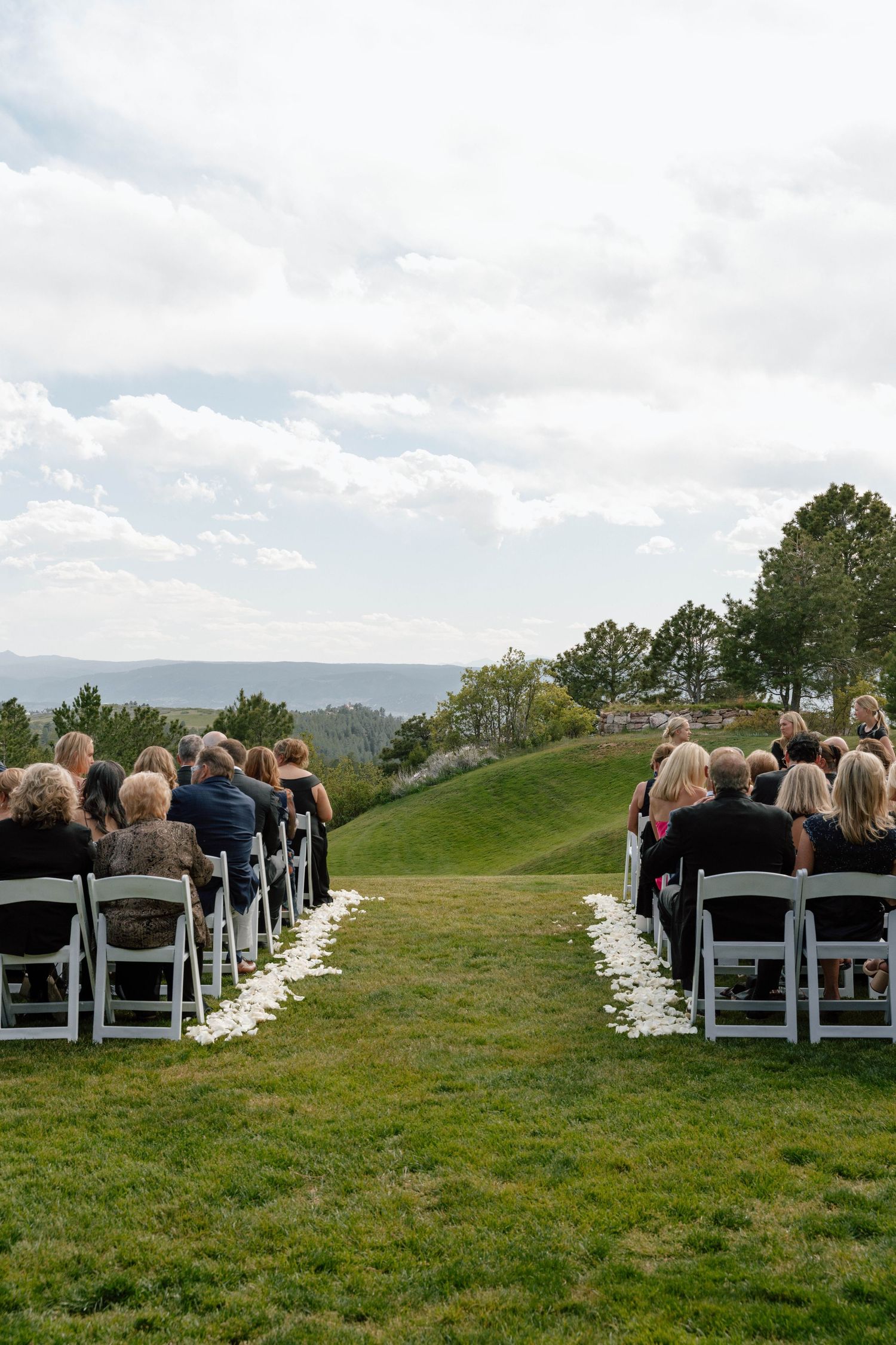 Outdoor wedding ceremony setup with white chairs arranged on a hillside overlooking scenic mountain views.
