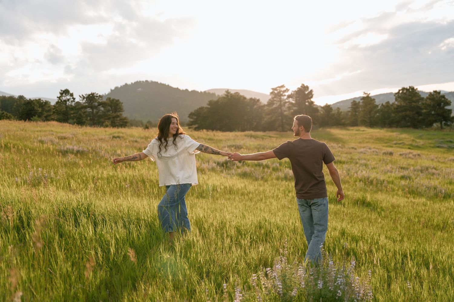 Panoramic view of a couple walking through a golden meadow with mountains in the background.