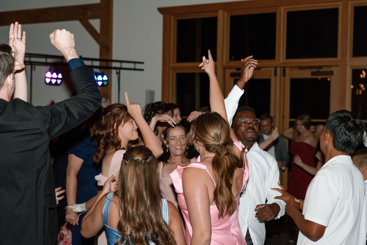 Guests dancing and celebrating at a lively indoor wedding reception with colorful DJ lights.
