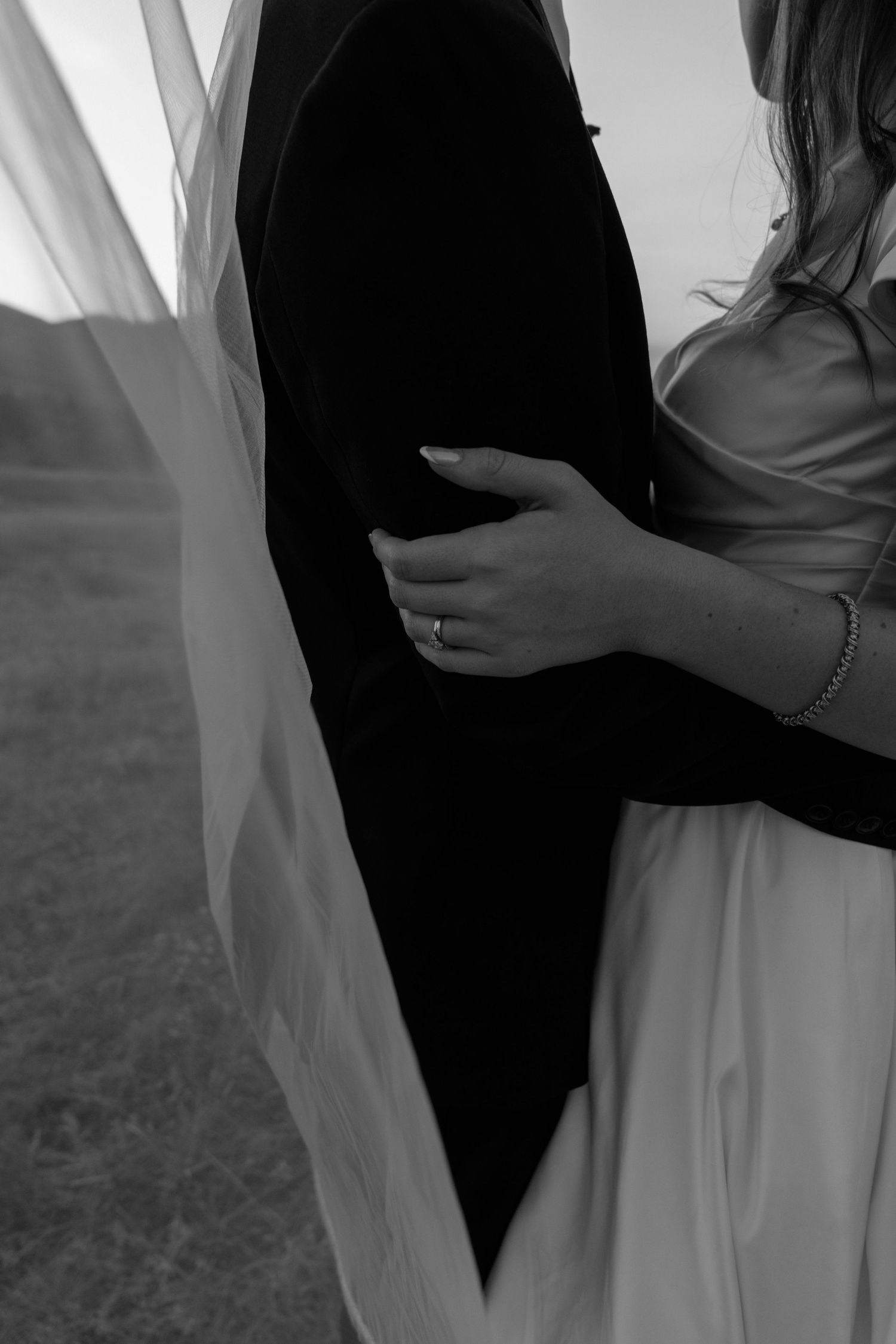 Artistic black and white shot of couple embracing, showing contrast between dark suit and white wedding dress.