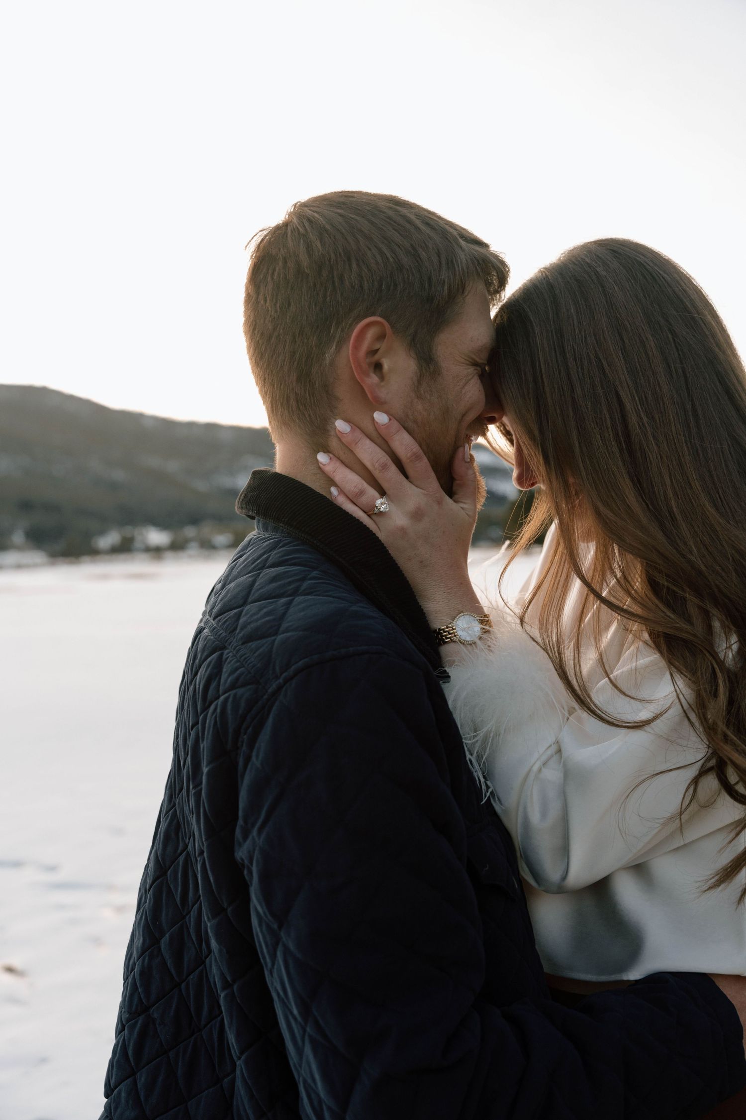 Intimate winter engagement photos with a snow-covered lake and mountains in the background.