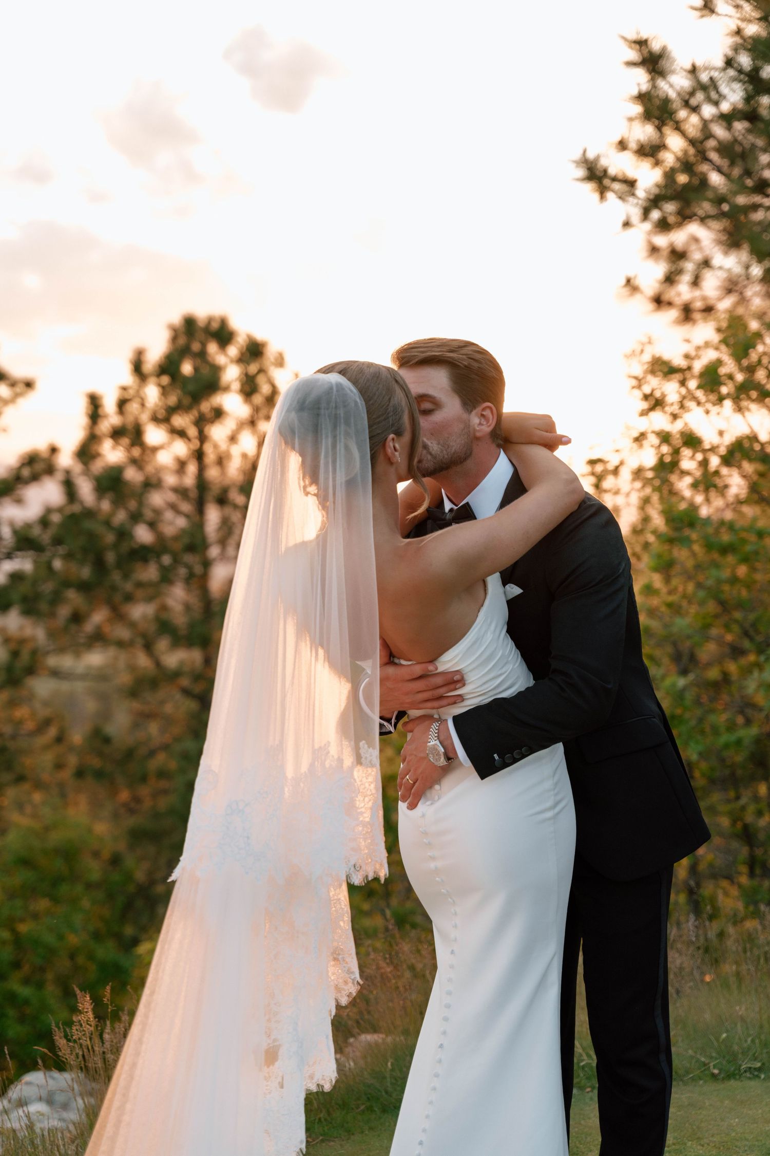 Romantic sunset portrait of newlyweds embracing with flowing veil in golden light.