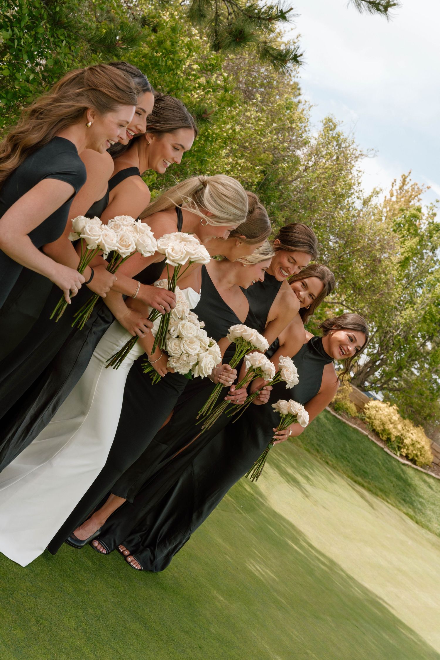 A group in formal attire holding white bouquets while standing in a line on a golf course.