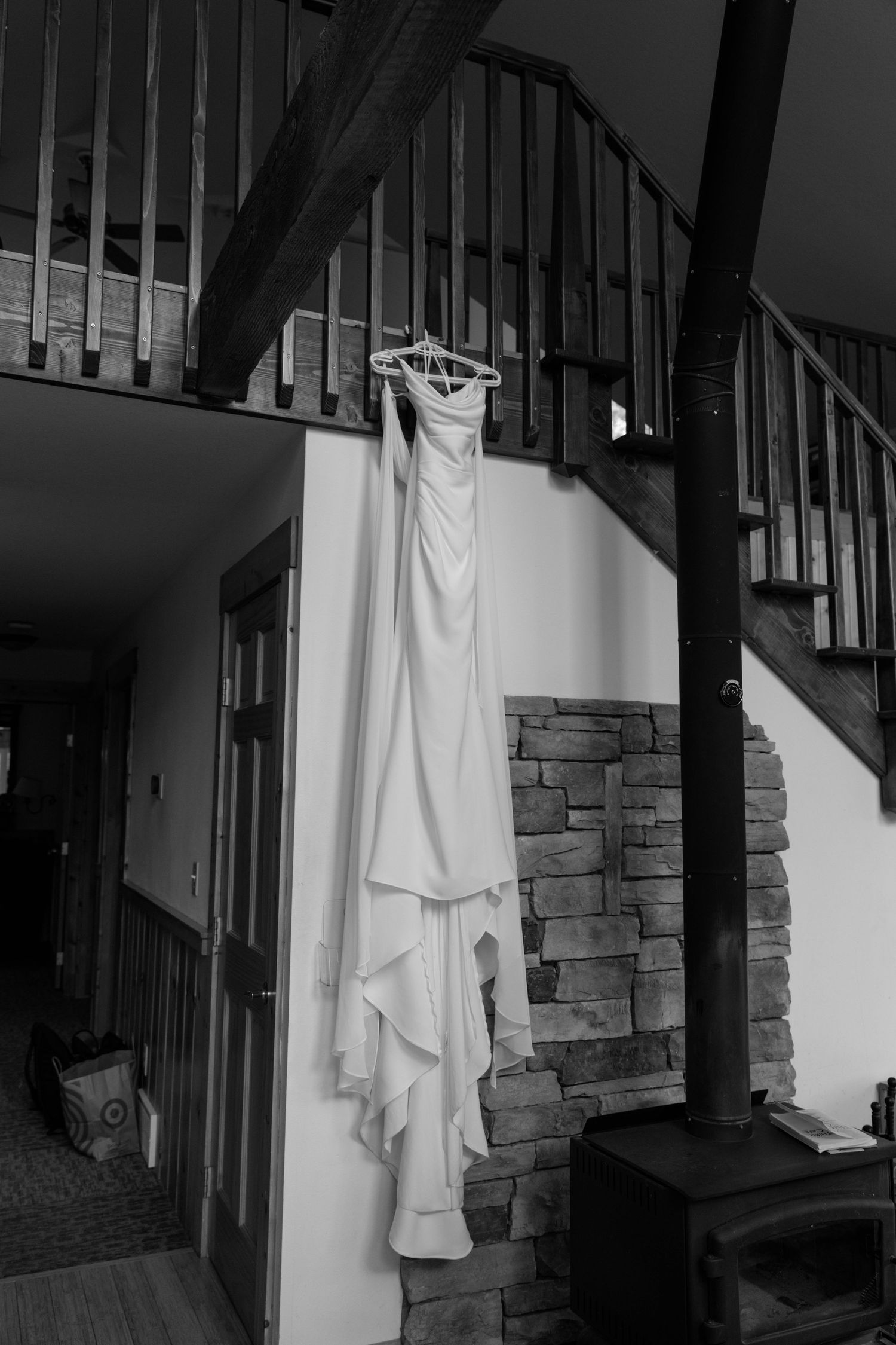 Elegant white wedding dress hanging on a hanger over a rustic staircase railing in a cozy lodge interior.