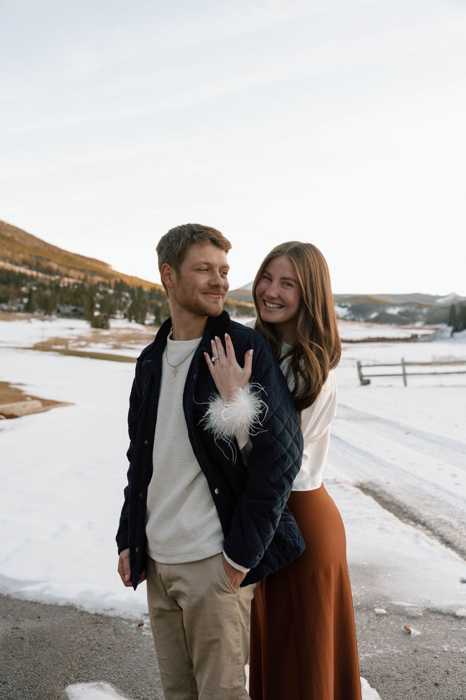 A couple laughs together during their engagement session in a snow-covered mountain setting.