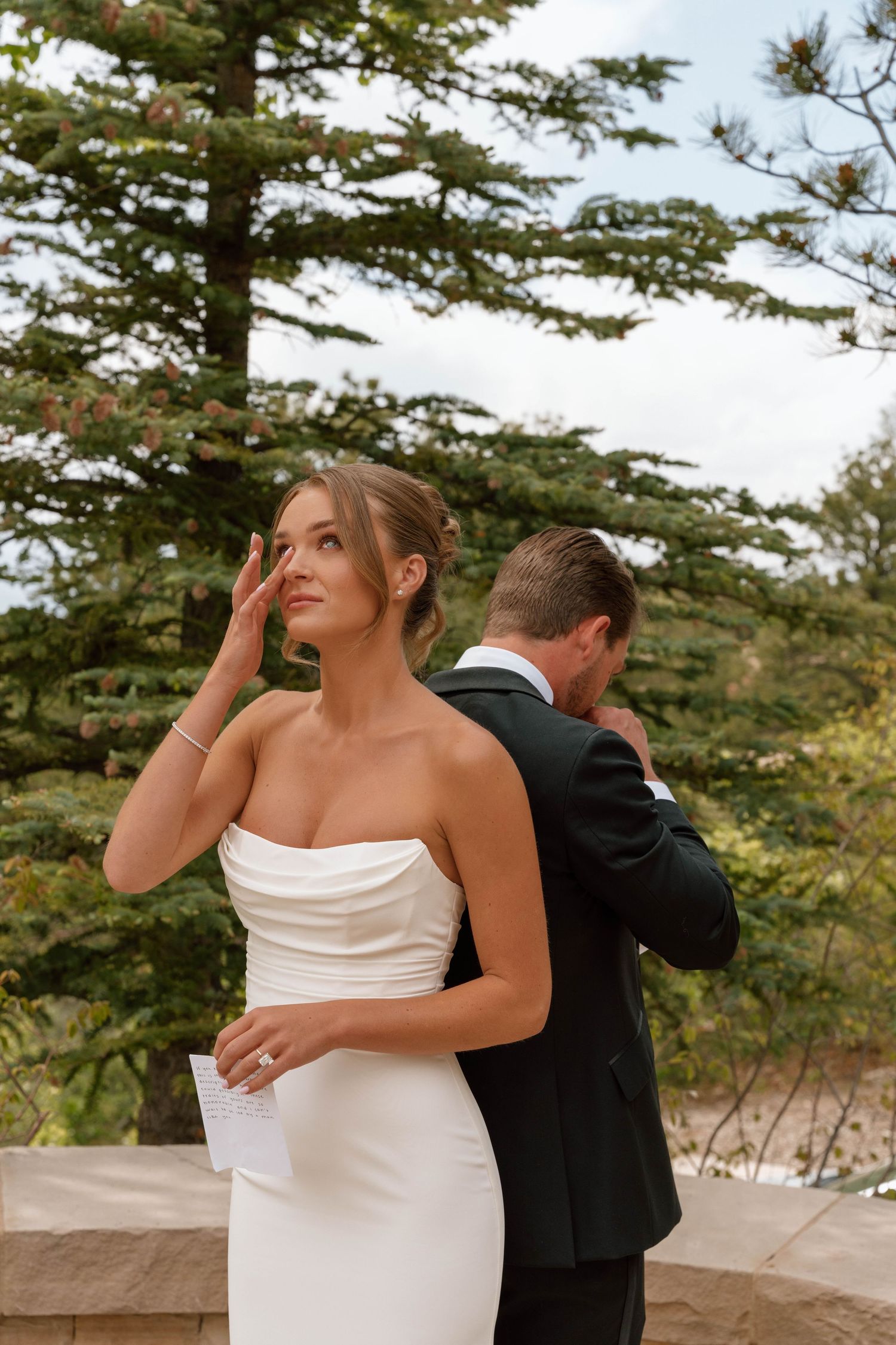 Elegant wedding moment captured on outdoor stone terrace with pine trees.