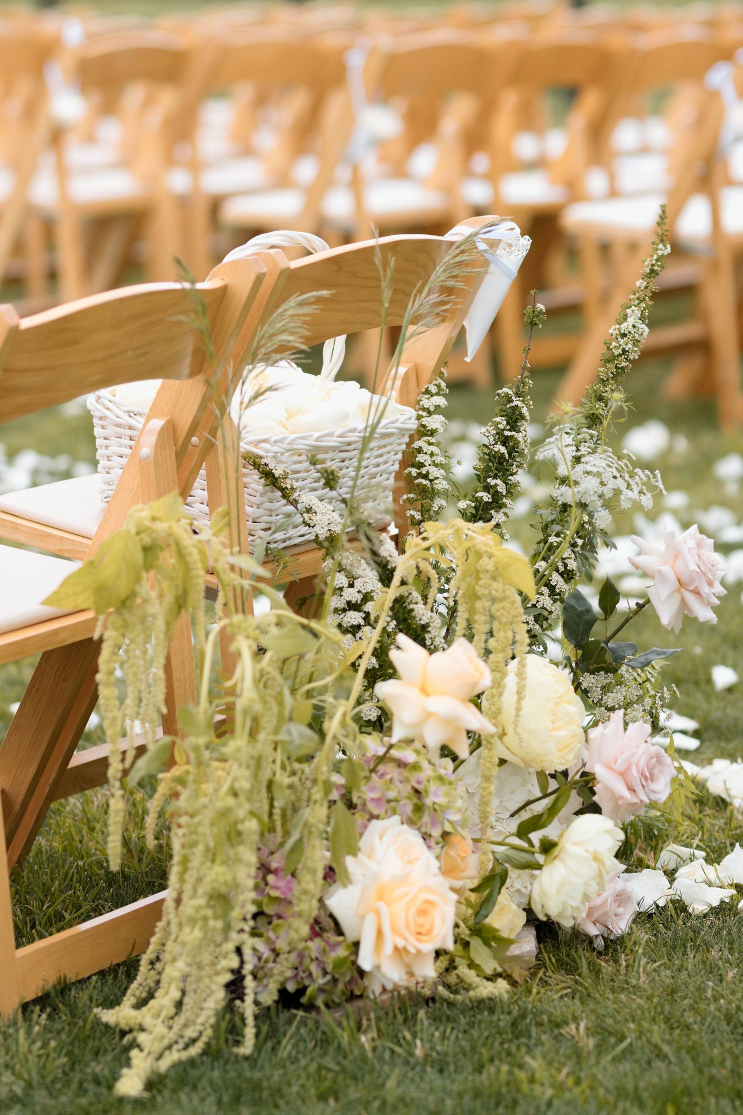 Wedding ceremony aisle decorated with white flowers and greenery along wooden chairs.