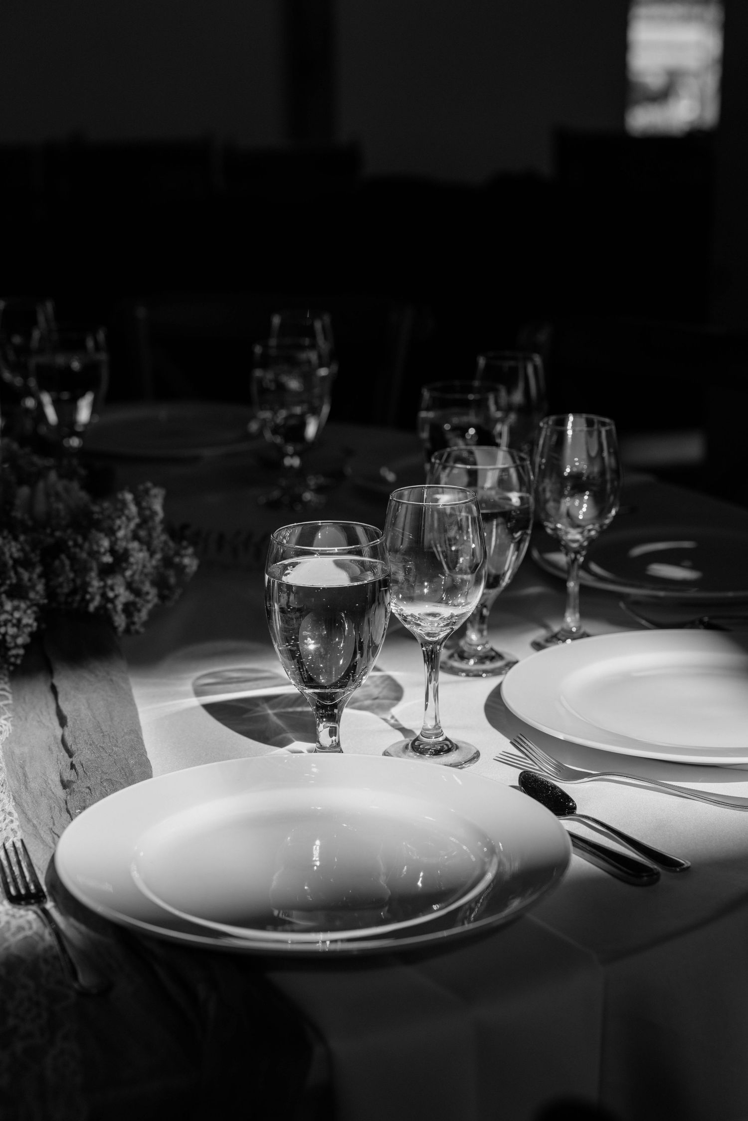 Elegant black and white photo of a formal wedding reception table setting with wine glasses and white plates.