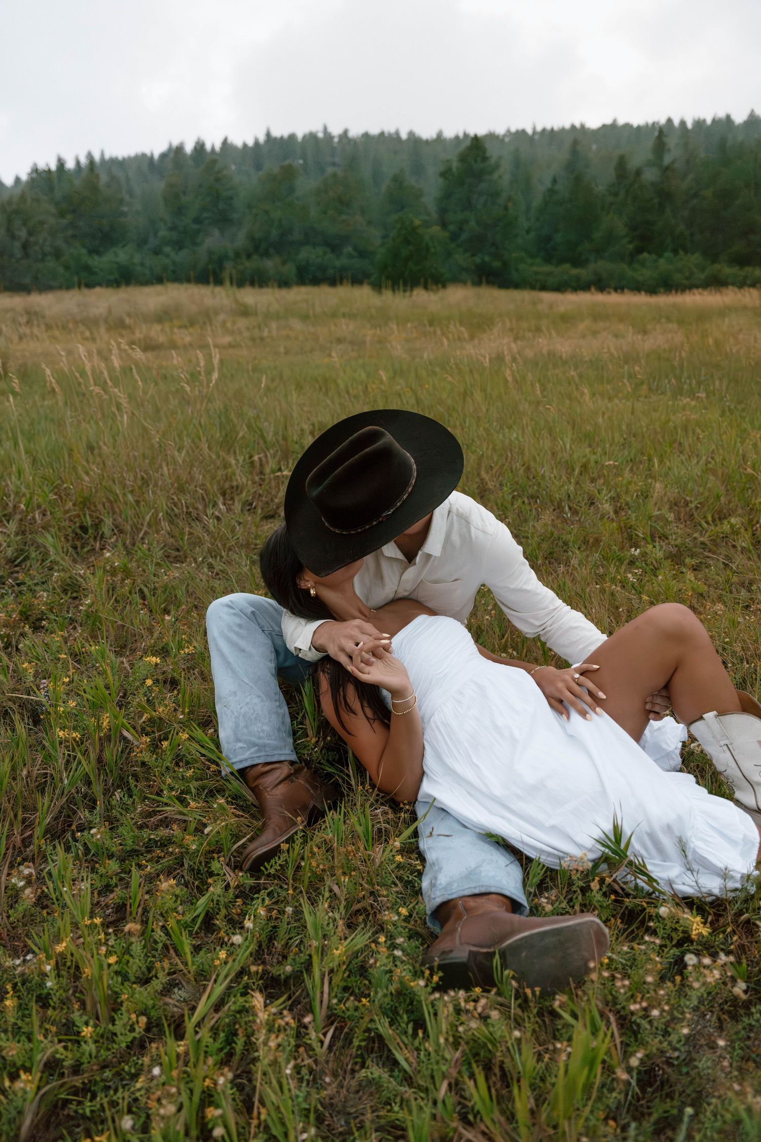 Intimate moment between couple in western wear lying in mountain meadow.