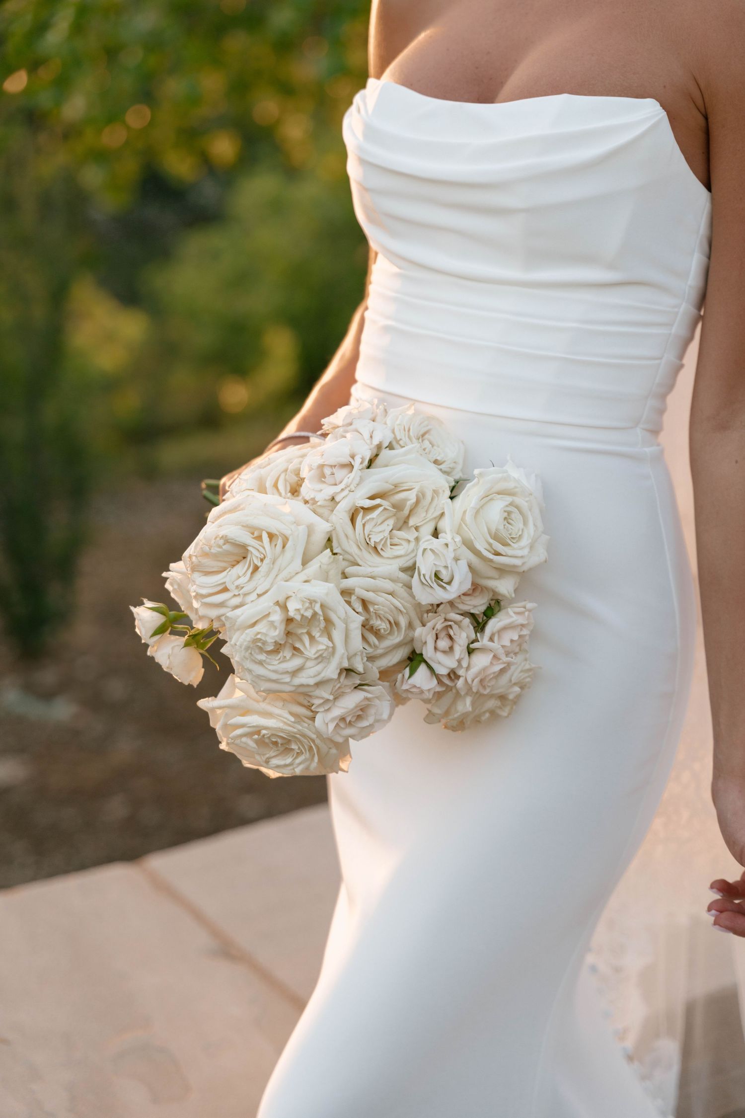 Close-up detail of a white wedding dress with elegant cream rose floral embellishments.