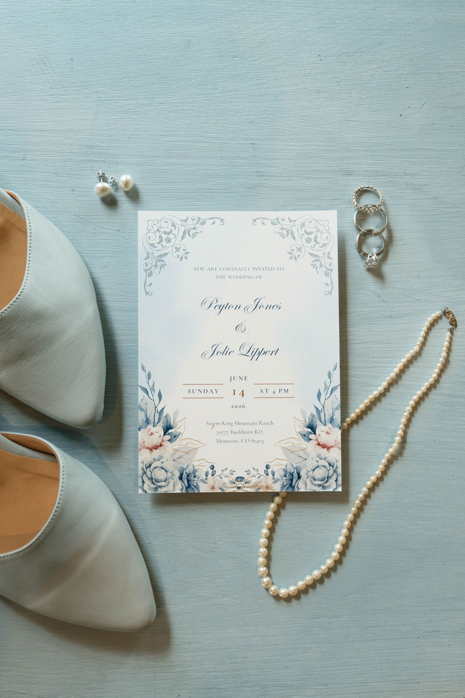 Elegant wedding invitation for Peyton Jones and Jolie Lippert displayed with pearl necklace, rings, earrings, and blue heels.