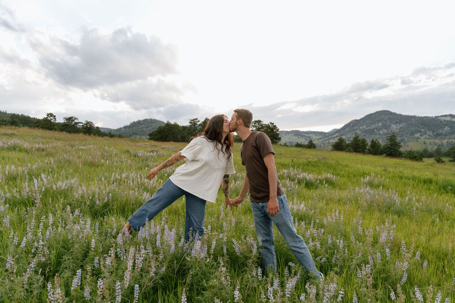 Two people dance and embrace in a field of purple wildflowers with rolling hills behind them.