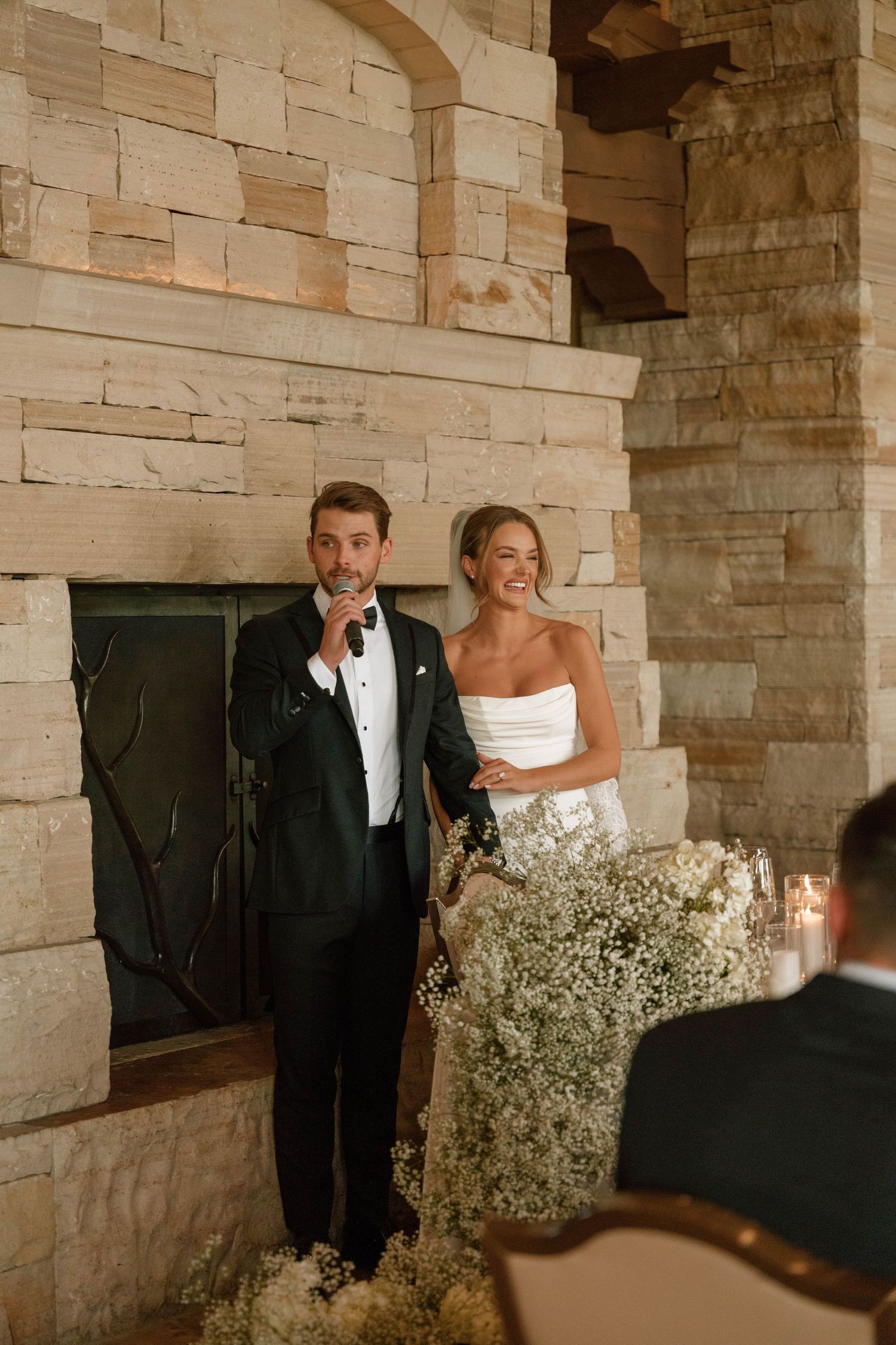 Wedding couple standing against stone wall with baby's breath floral decorations.