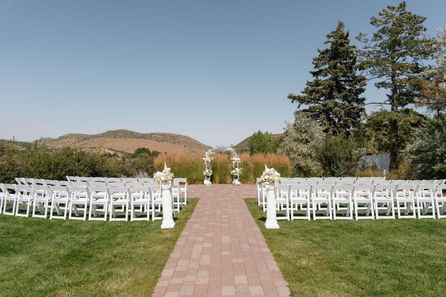 Outdoor wedding ceremony setup with white chairs on grass overlooking mountain landscape.