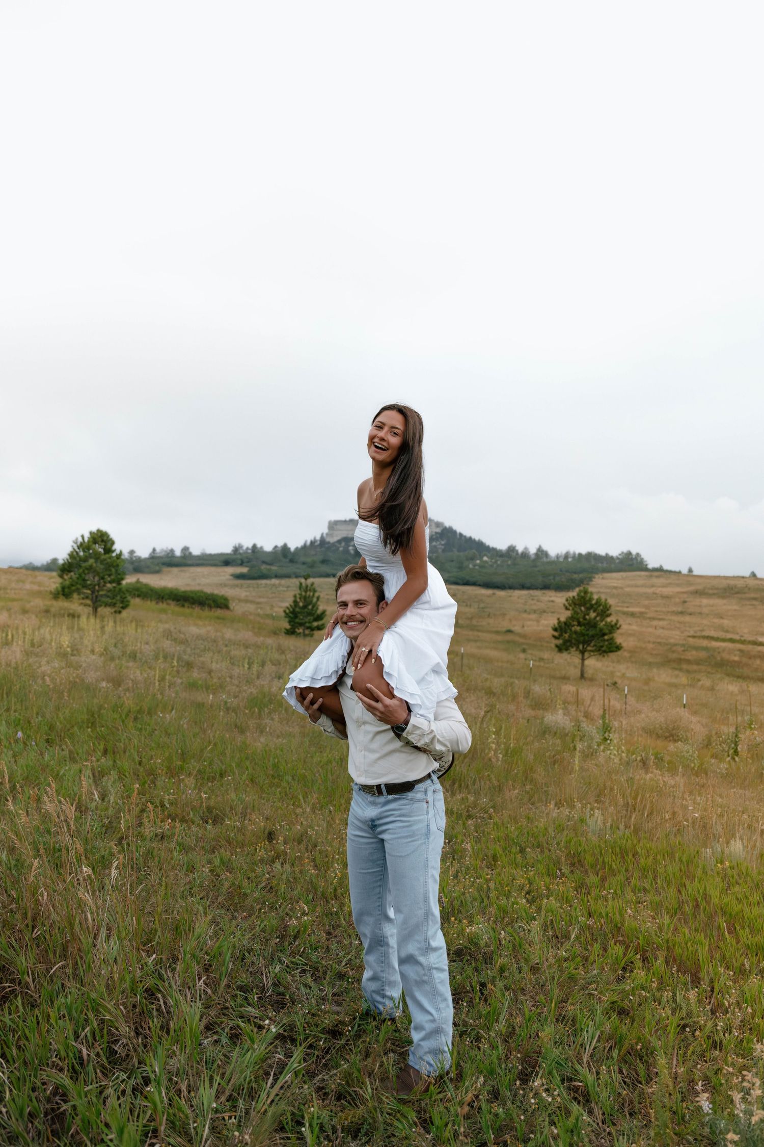 A playful lift pose in a mountain meadow with casual western attire.