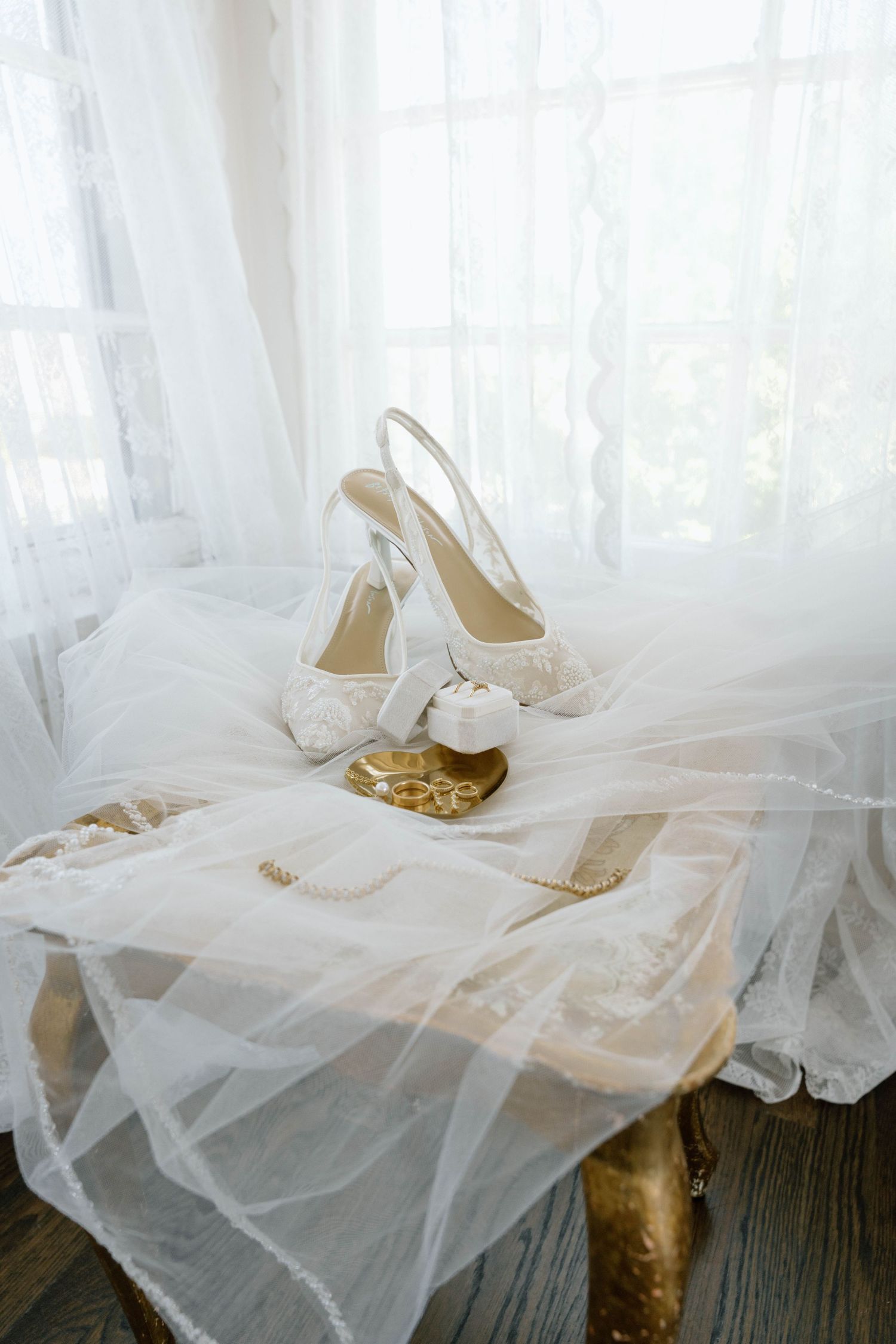 Elegant white lace bridal shoes and veil arranged on a vintage surface with delicate tulle fabric.
