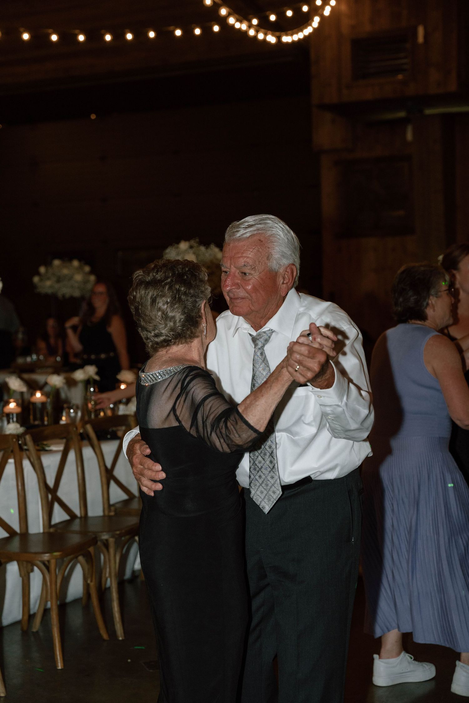 Wedding reception dance floor filled with couples dancing under warm string lights.