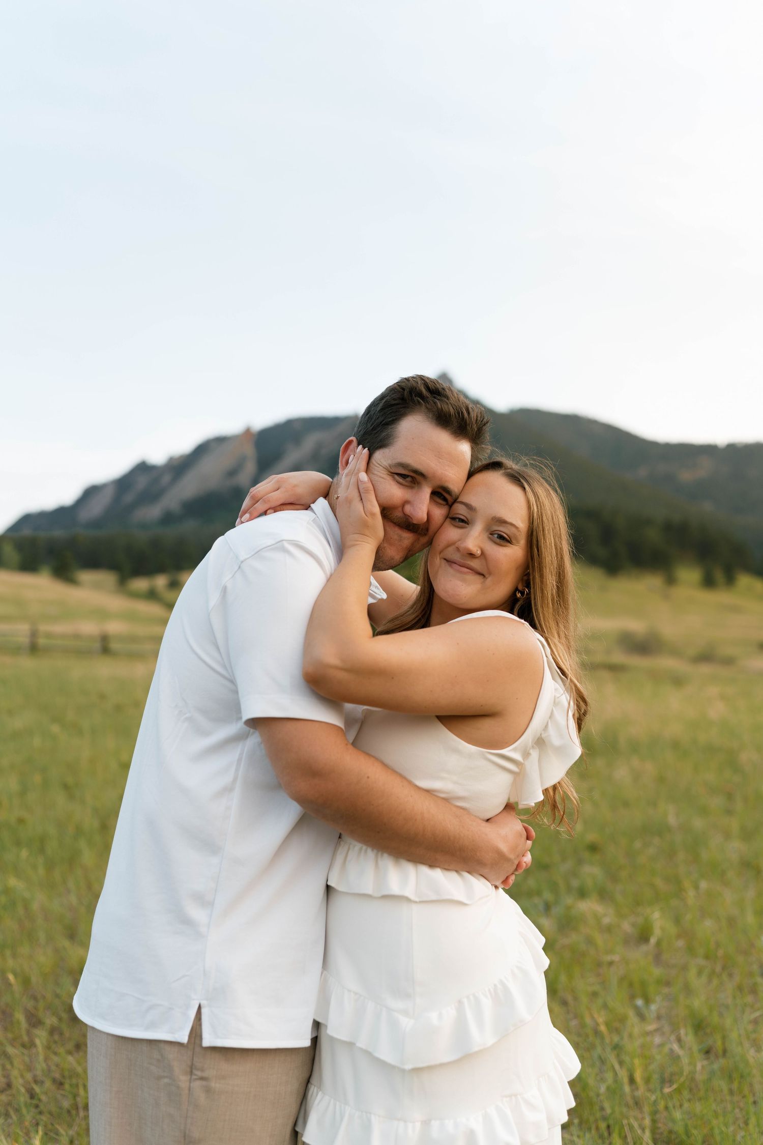 Happy couple hugging and smiling in a green meadow with rocky mountain formations in the background.