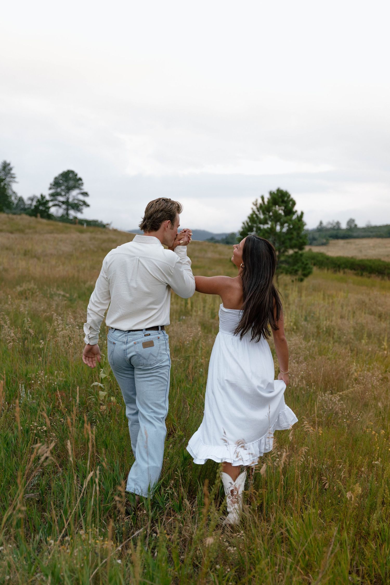A couple walking hand in hand through tall grass in a mountain meadow.