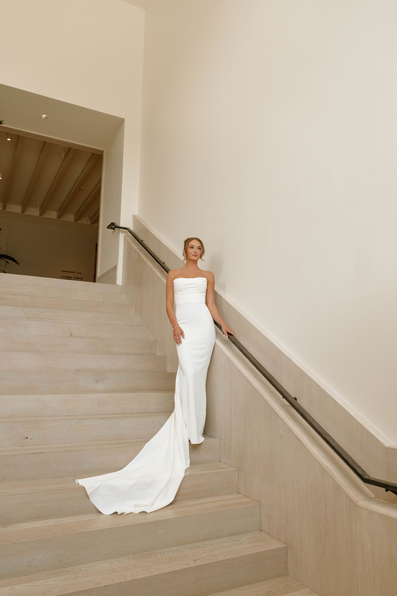 An elegant bride in a fitted white gown poses on modern concrete stairs with flowing train.