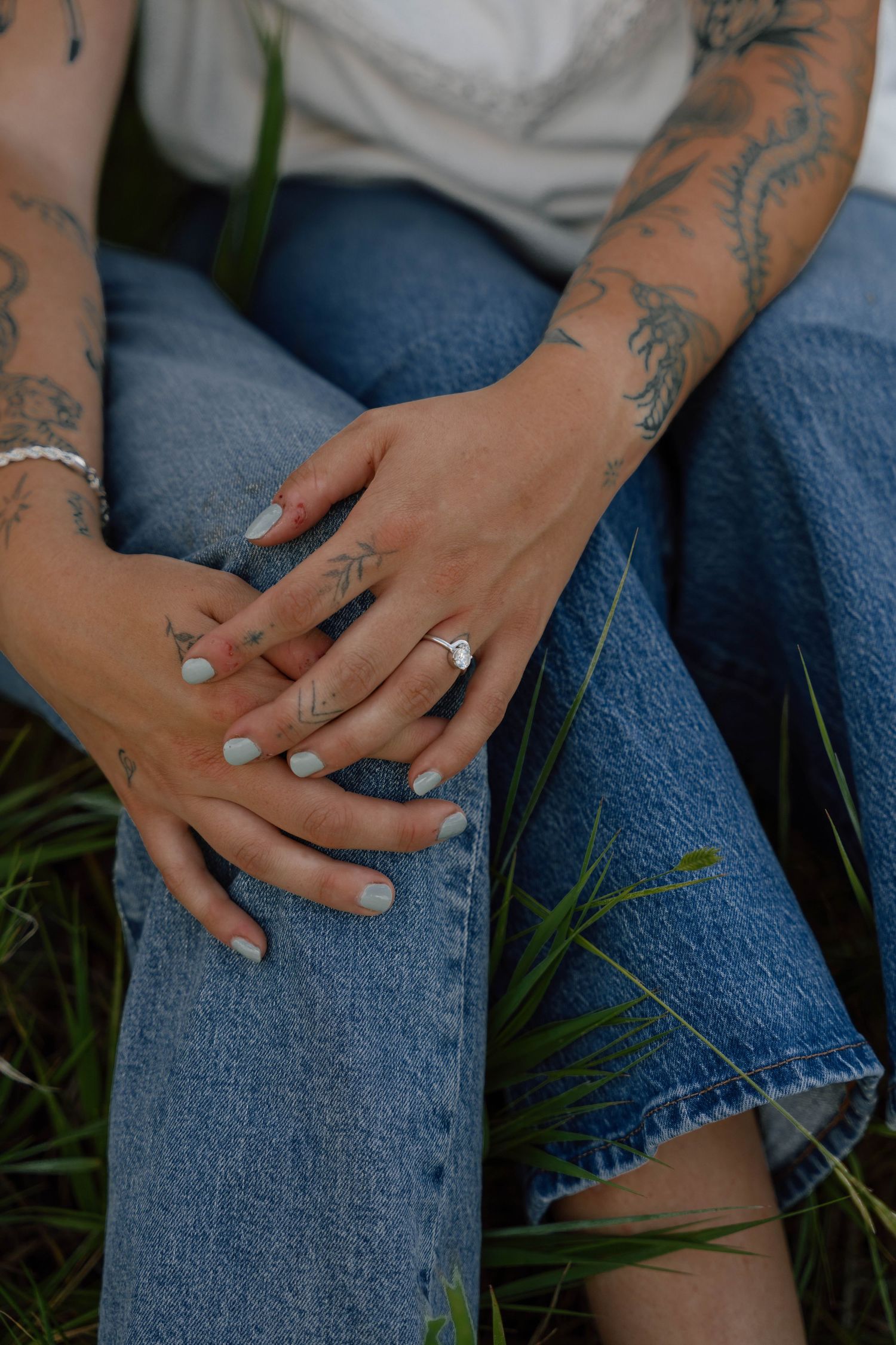 Close-up of tattooed hands resting on blue denim jeans in a grassy field.