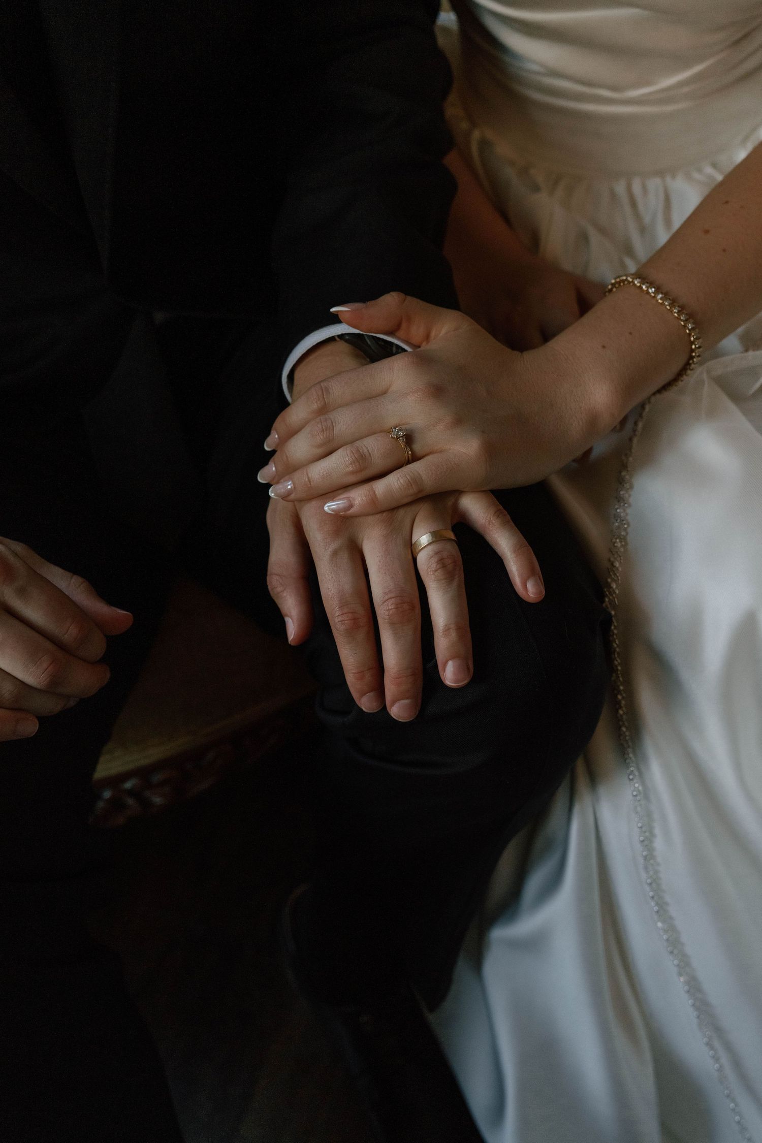 Close-up detail of hands resting on white wedding dress fabric.