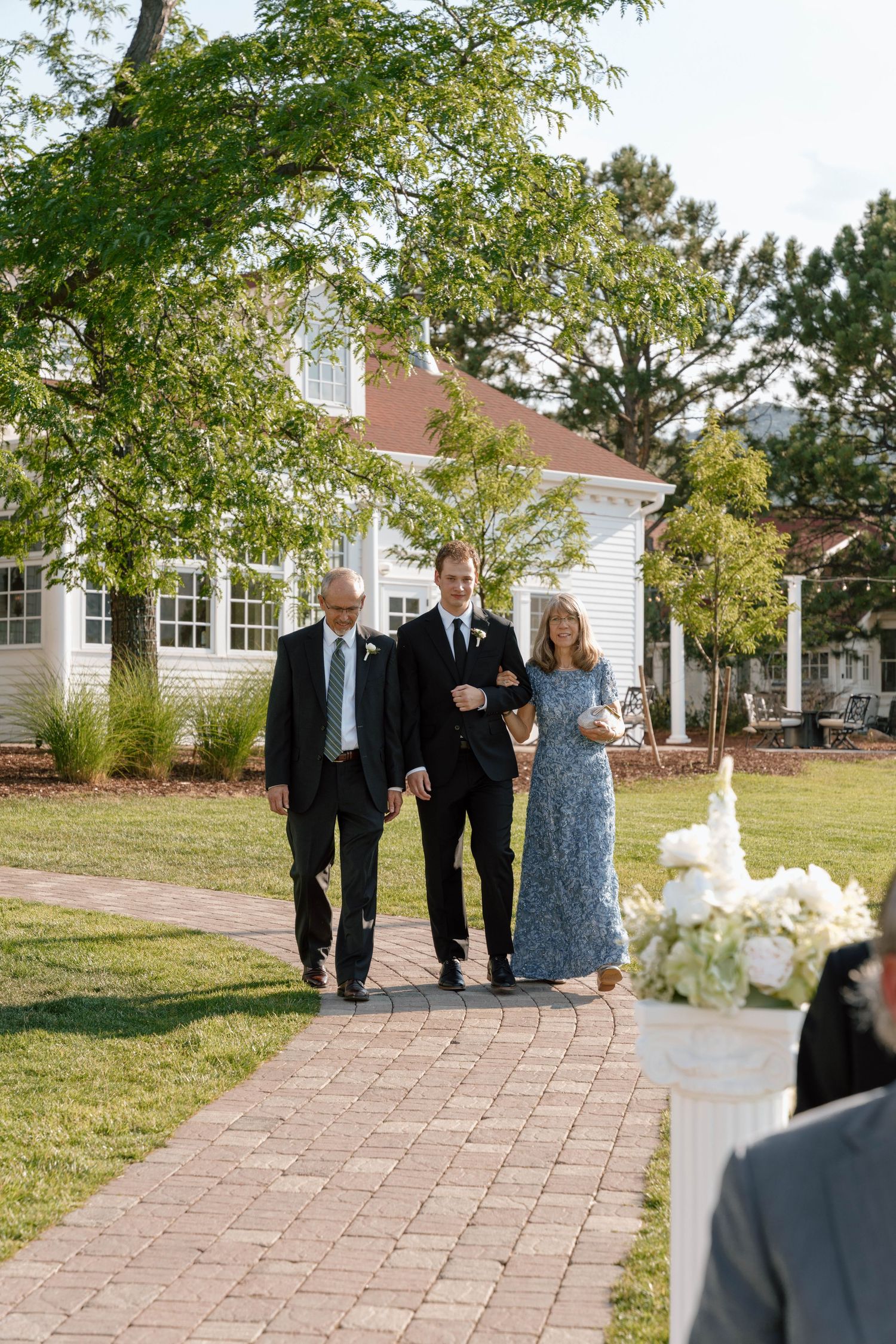 Wedding party walks along a brick pathway towards a white colonial-style building.