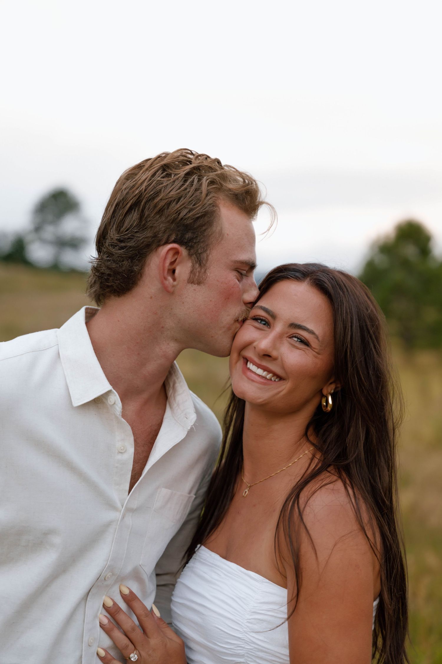 A romantic moment shared between a couple in a sunlit meadow wearing white outfits.