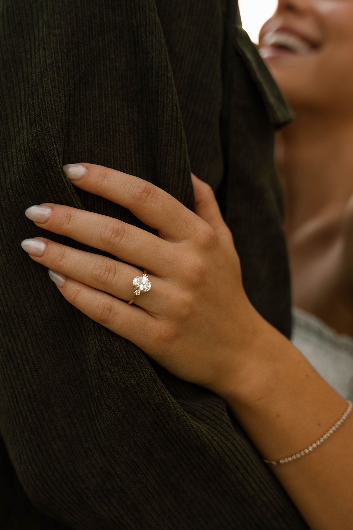 Close-up of a woman's hand displaying a stunning solitaire diamond engagement ring while embracing a partner.