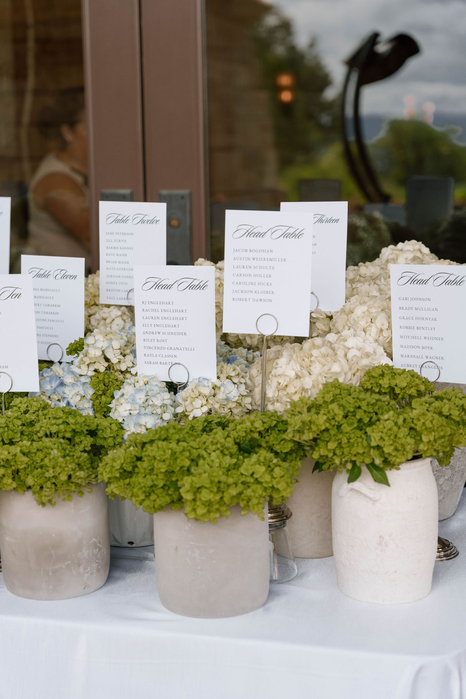 Wedding seating cards displayed in concrete vases with white hydrangeas and green moss.