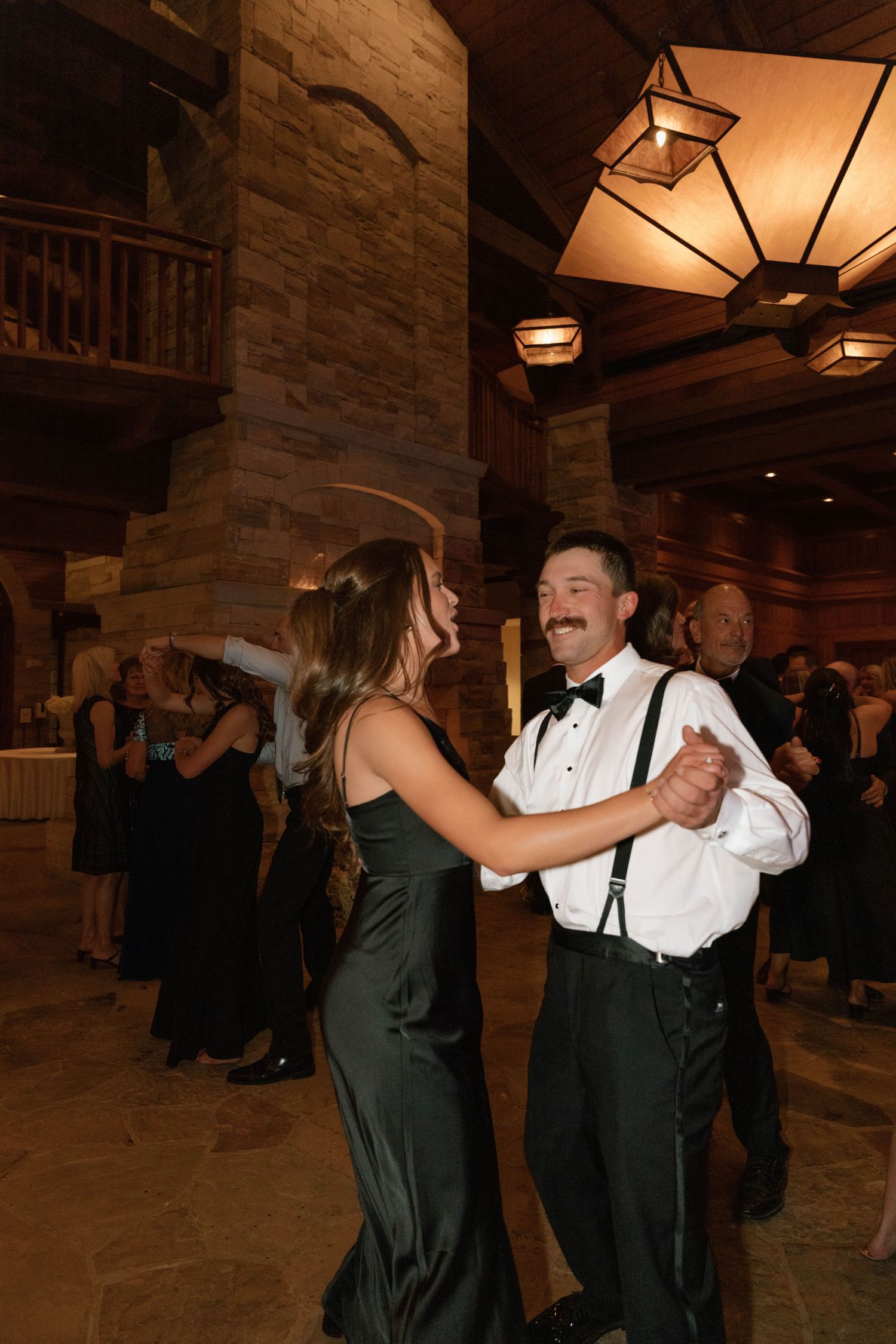 Couples dancing at a formal wedding reception in a rustic venue with stone walls.