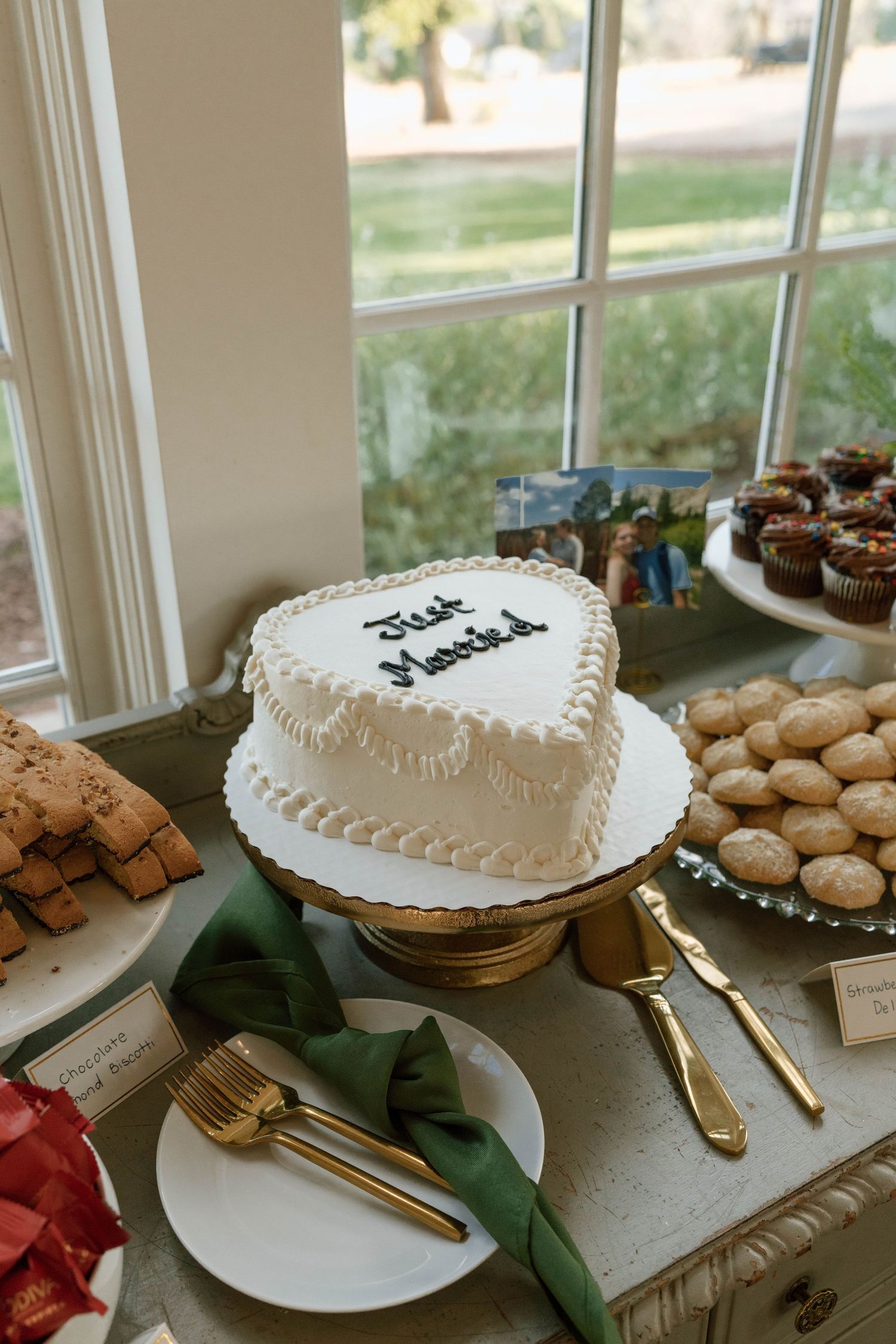 Heart-shaped wedding cake and dessert display with gold utensils on a white tablecloth.