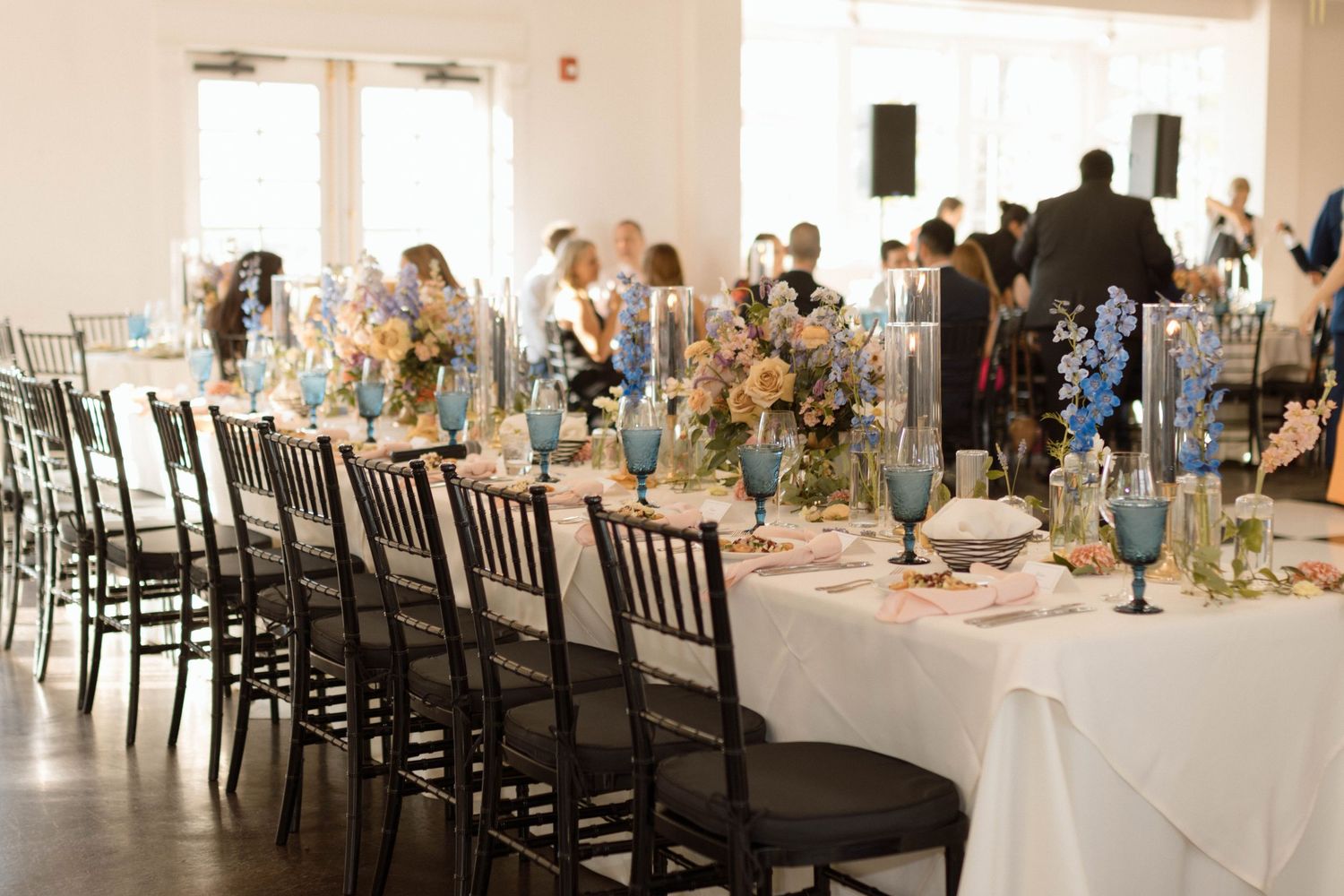 Long banquet tables set with white linens and blue glassware in a bright reception hall.