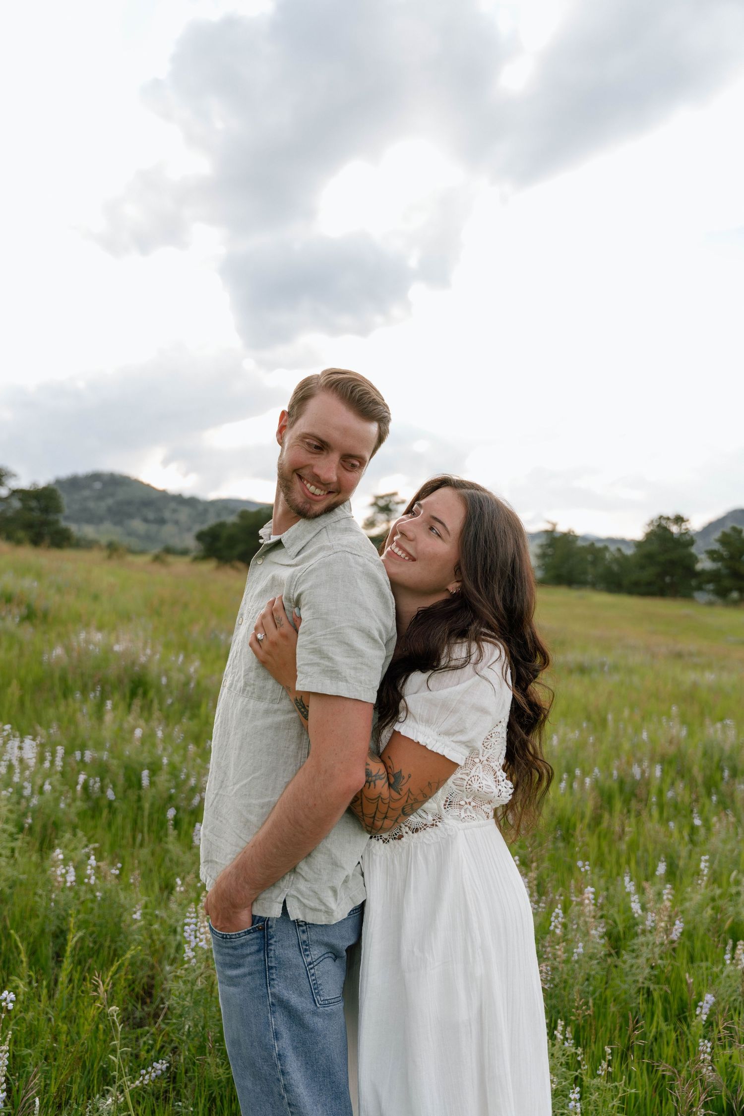 Couple embraces while laughing together in a mountain meadow filled with summer wildflowers.