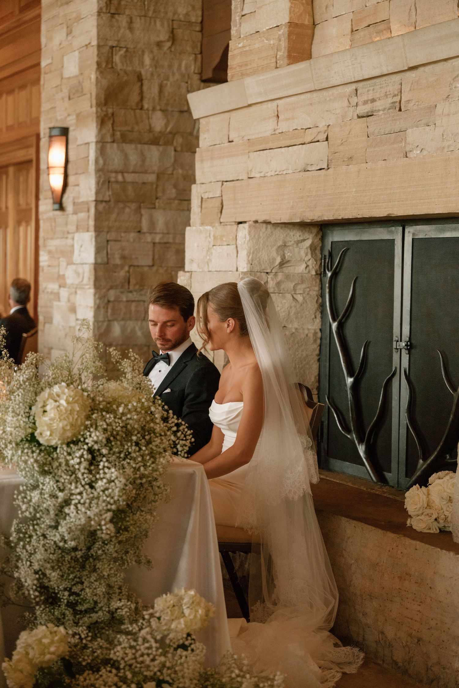 Wedding couple sharing intimate moment against stone wall decorated with baby's breath flowers.