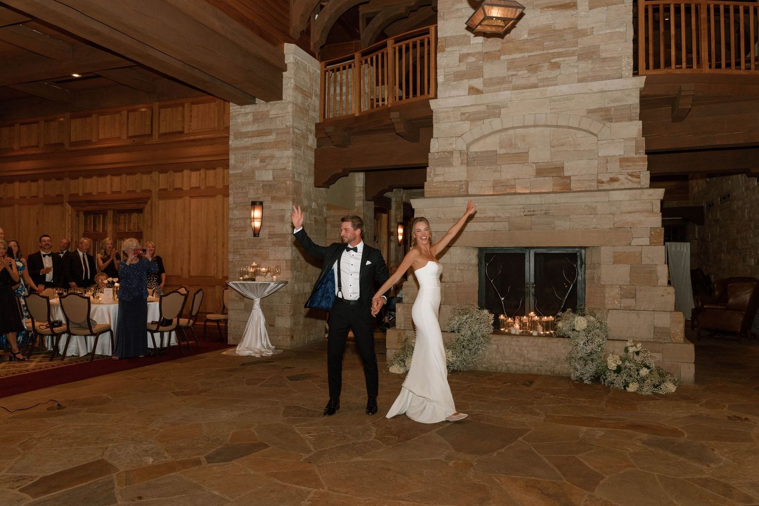 Wedding guests dance and celebrate at a rustic venue with stone walls and wooden beams.