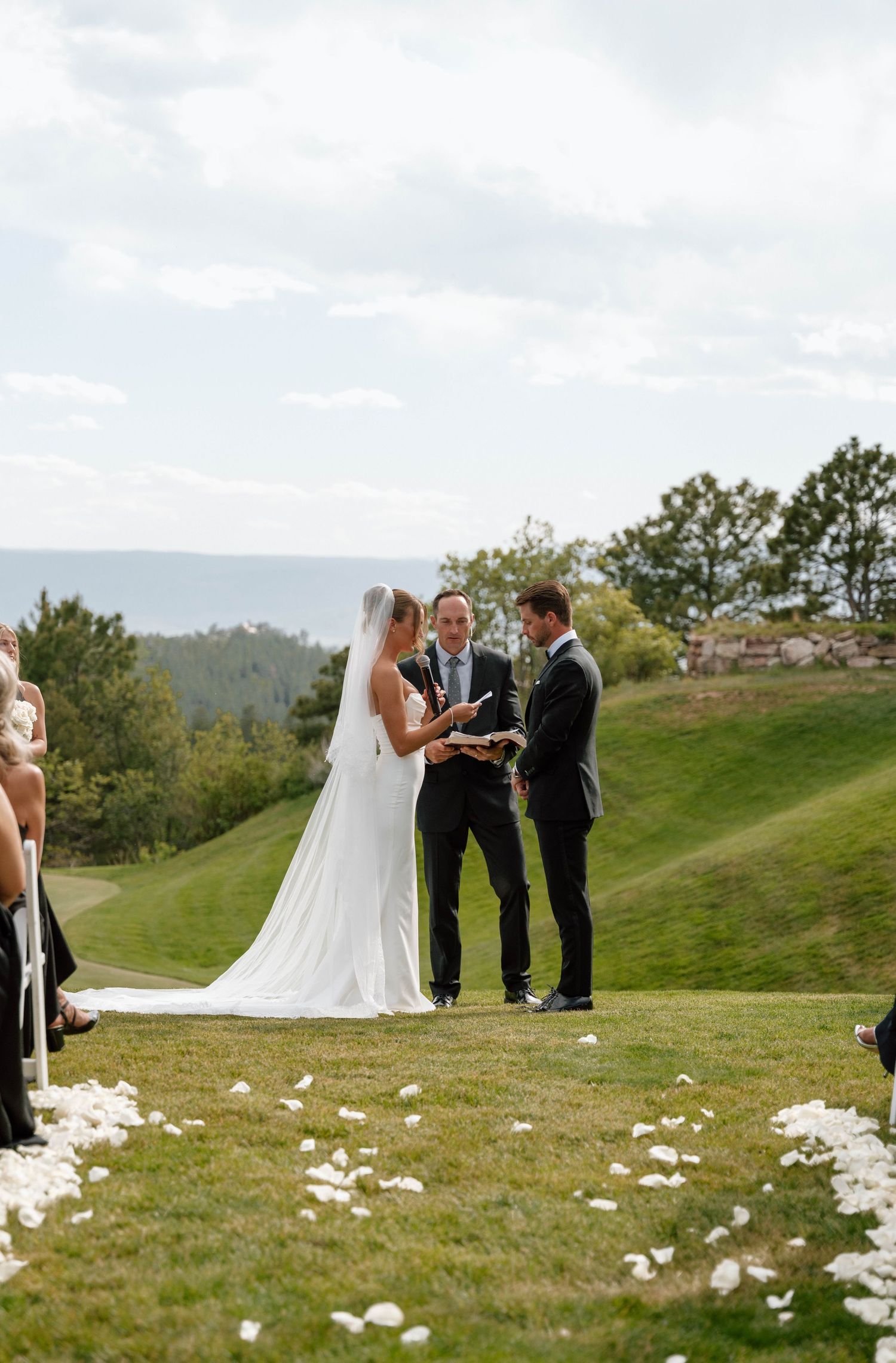 Mountain view wedding ceremony with white flower petals scattered along grassy aisle.