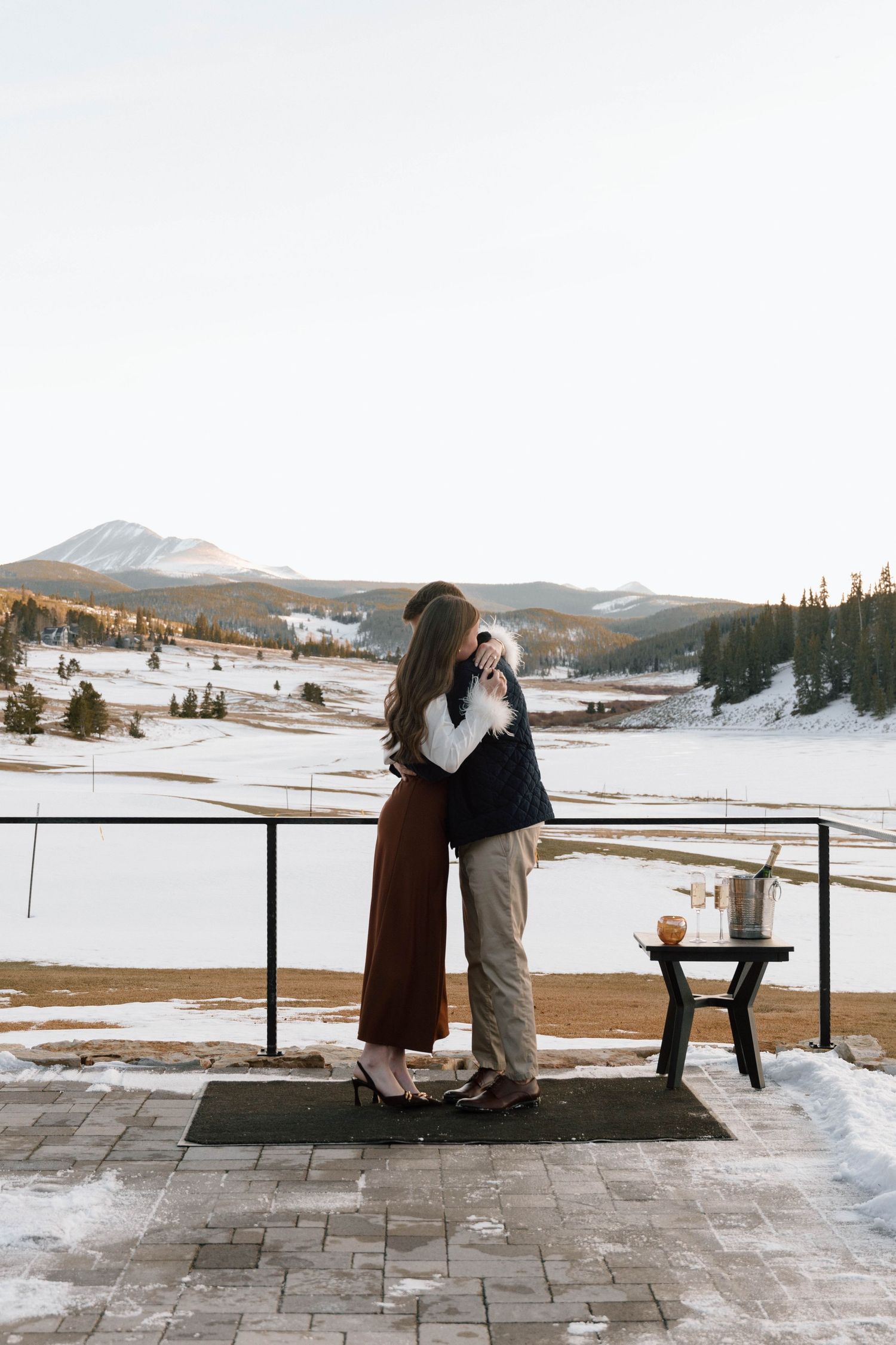 Couple sharing a romantic moment on a terrace overlooking snow-covered mountains.