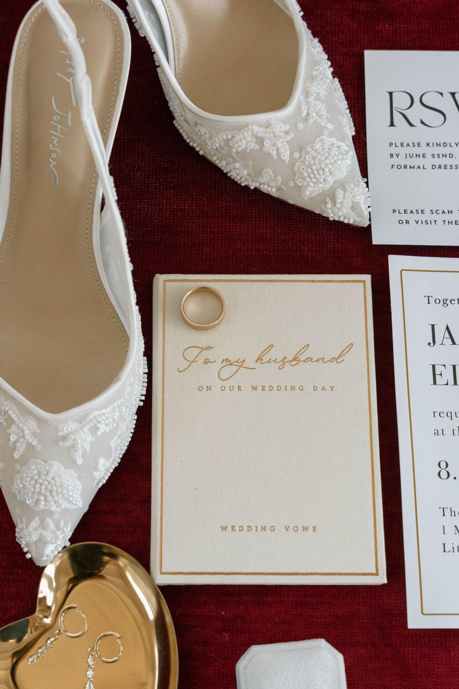 White lace bridal shoes next to wedding stationery and a gold-lettered card reading 'To my husband'.