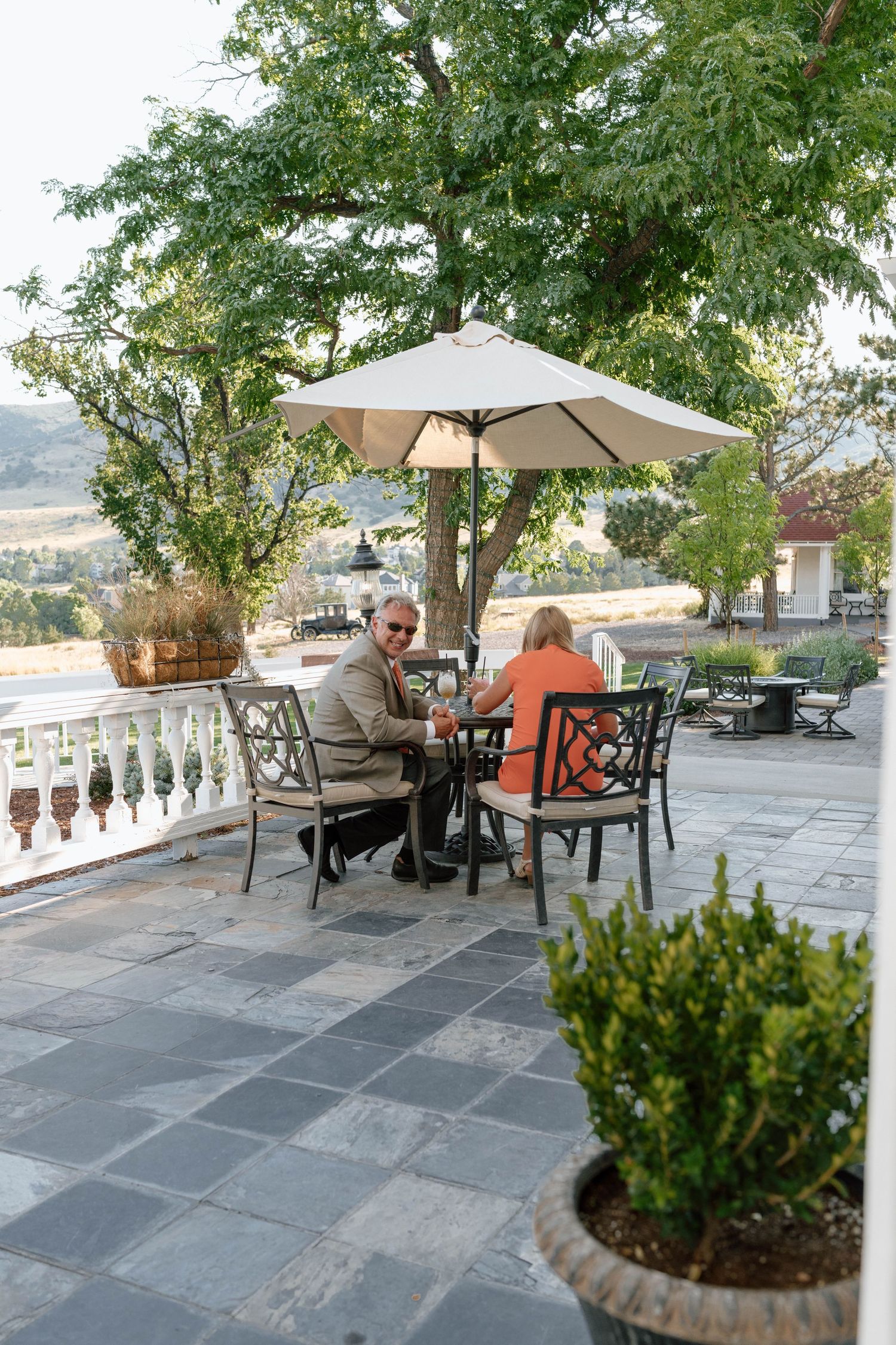 Outdoor seating area with umbrellas and stone balustrade overlooking mountain views.