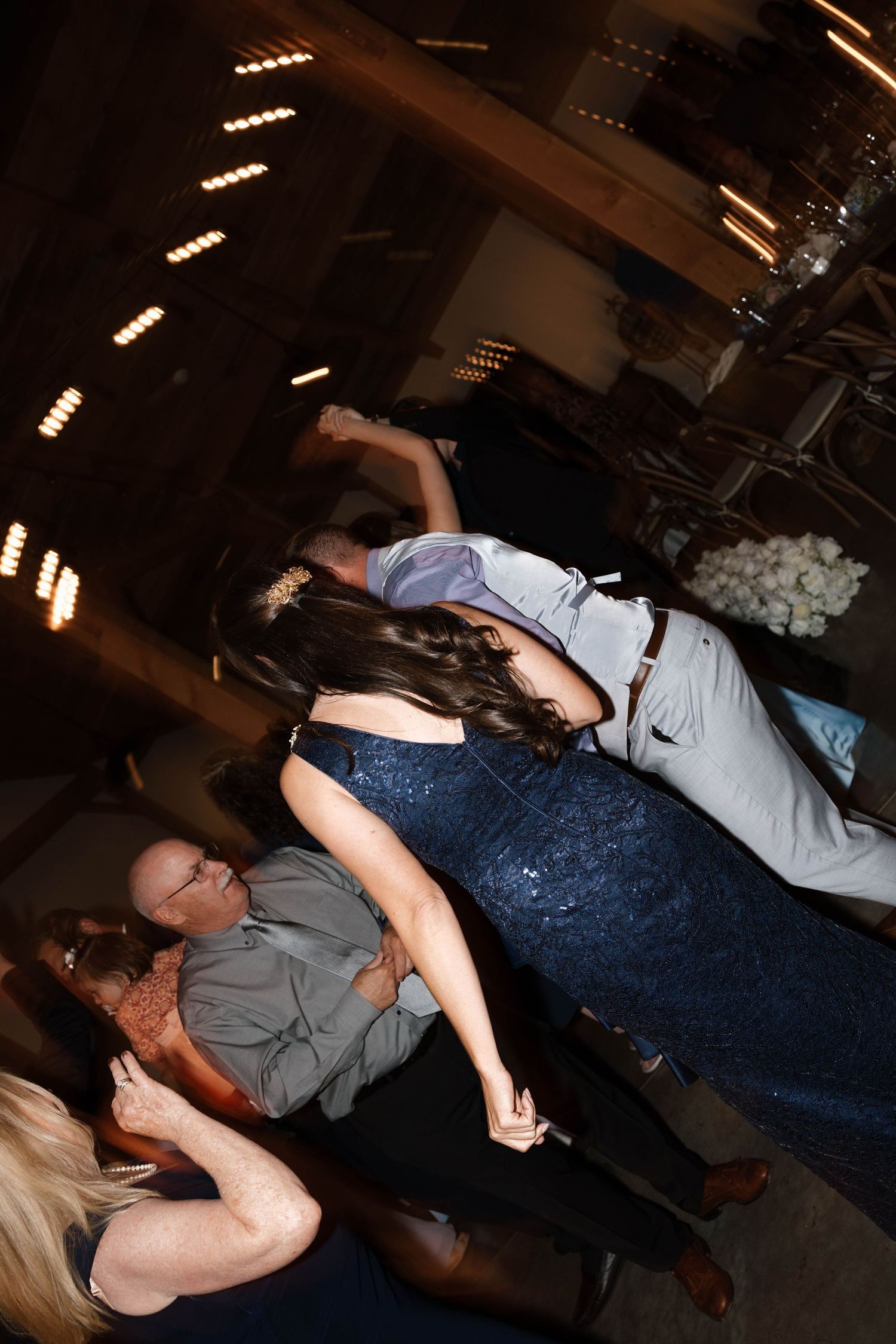 Wedding guests dancing energetically on dimly lit barn reception dance floor.