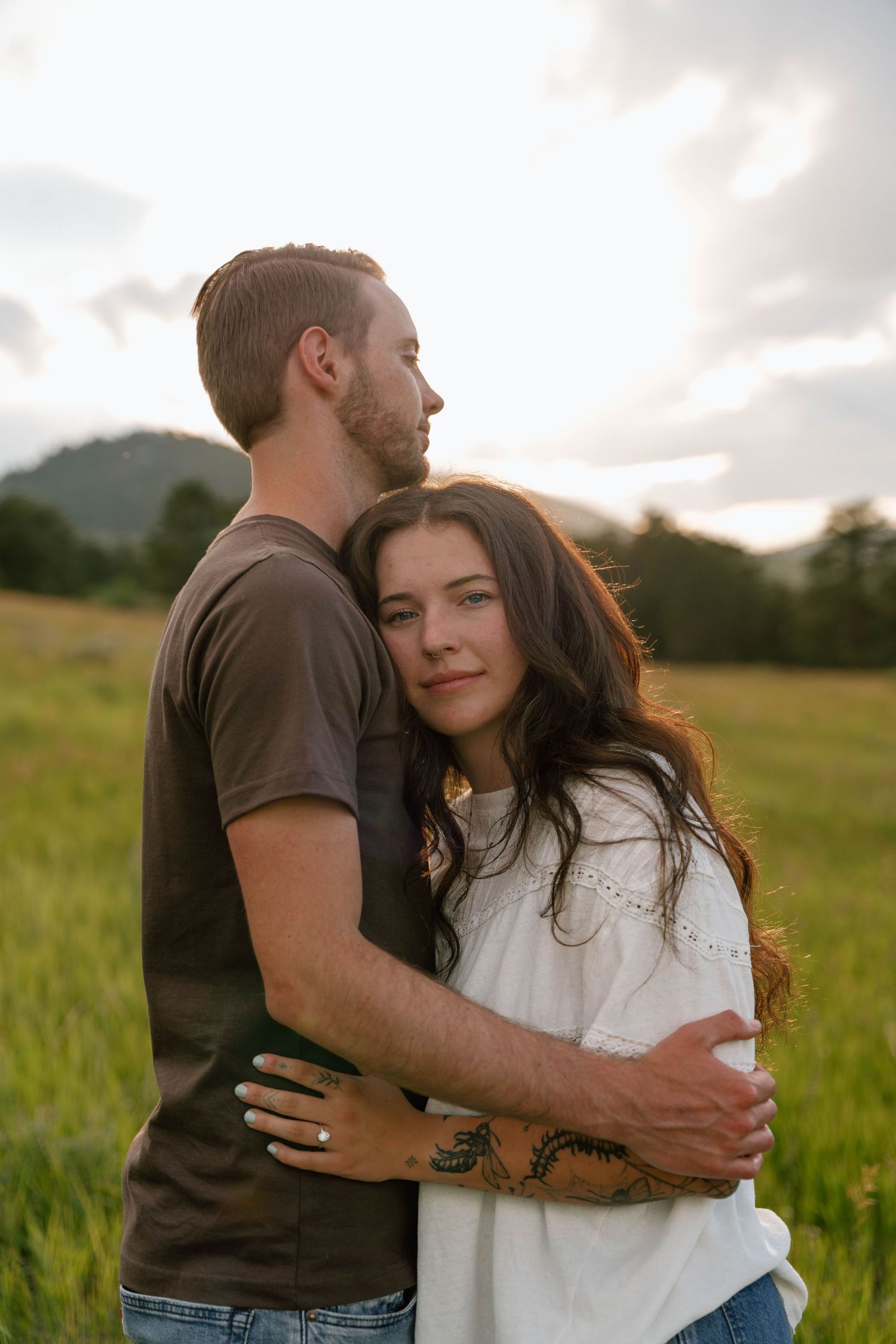 Intimate embrace between two people in casual attire standing in a wildflower meadow at sunset.