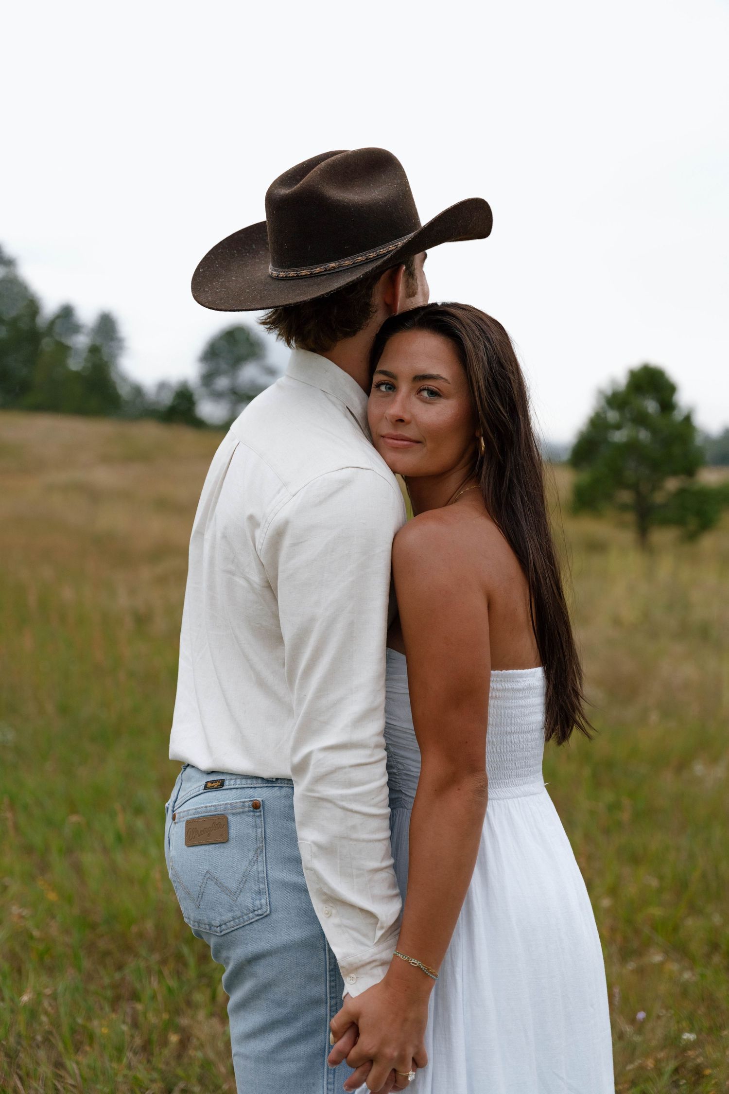 A tender embrace between a couple in western attire standing in a golden meadow.