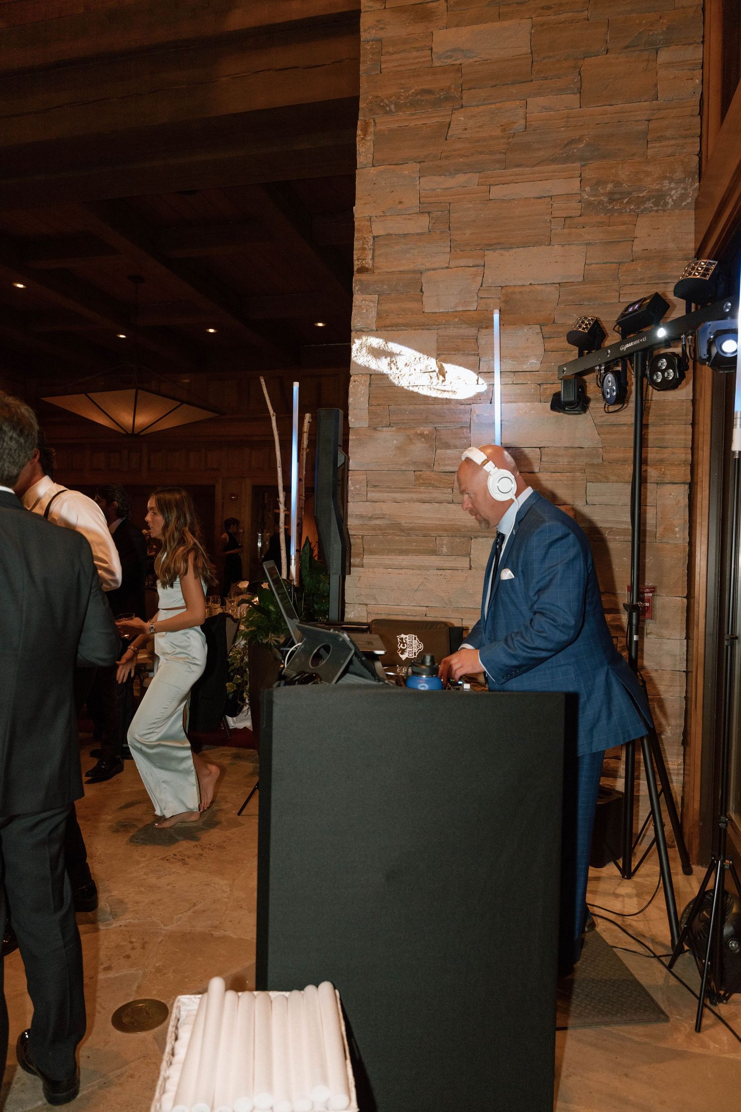 Wedding guests dance near a DJ booth setup at a rustic stone-walled venue.