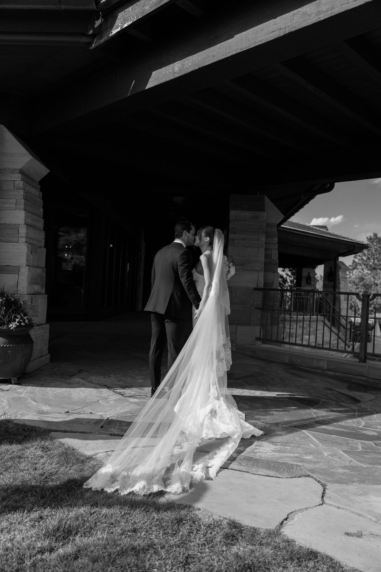 A flowing white wedding dress train trails elegantly across a stone pathway in dramatic black and white.
