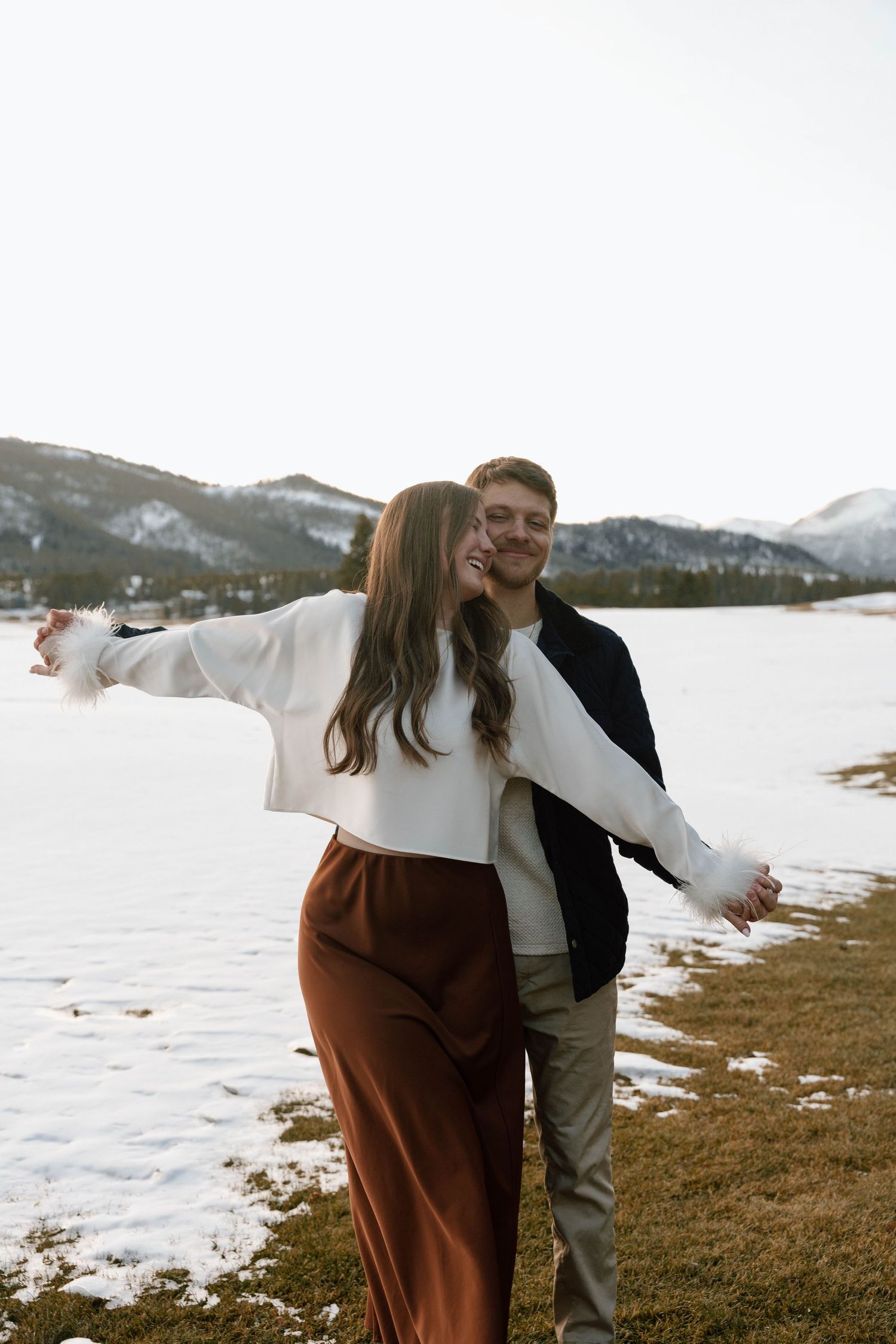 Joyful couple laughing together during their winter mountain photoshoot.
