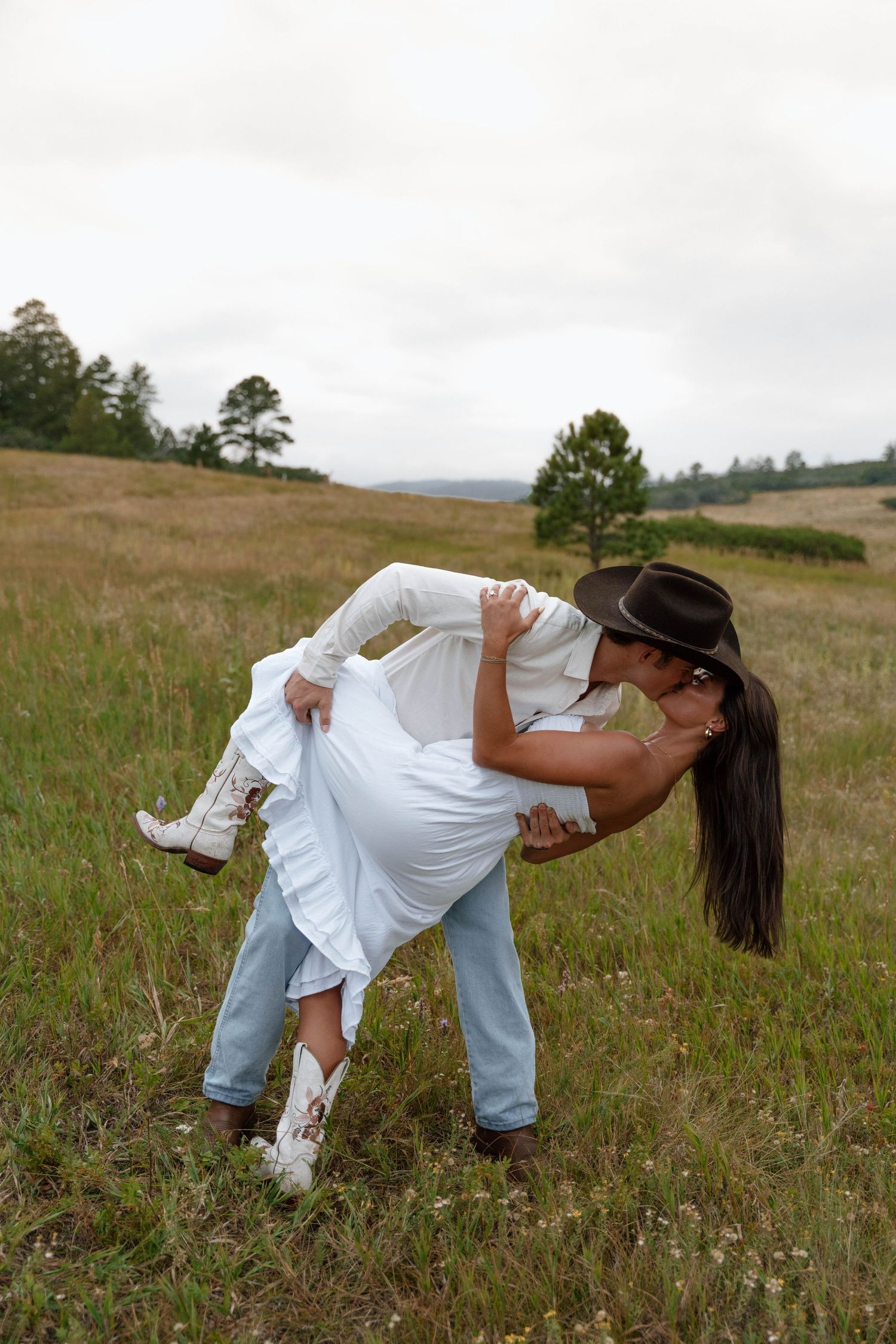 A romantic dip pose in a rustic field with mountains in the background.